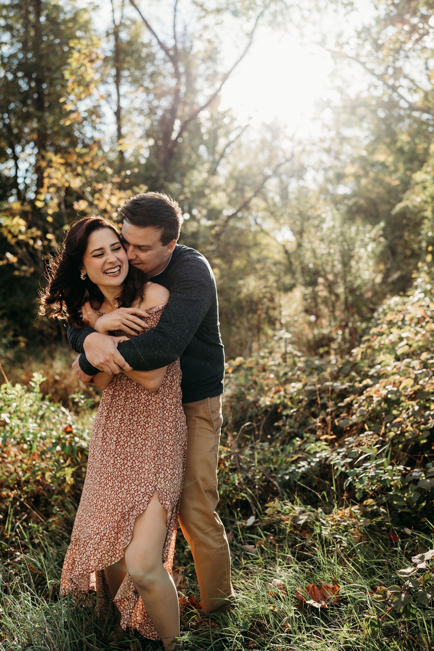 A couple sharing a playful embrace in a sunlit forest clearing.