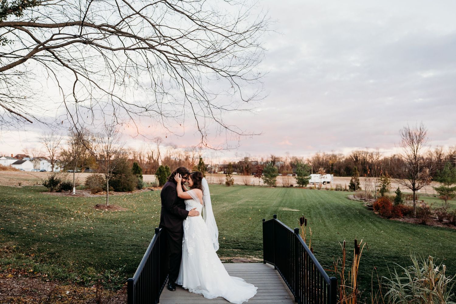 Bride and groom share a romantic kiss on a bridge at sunset during their outdoor wedding ceremony.