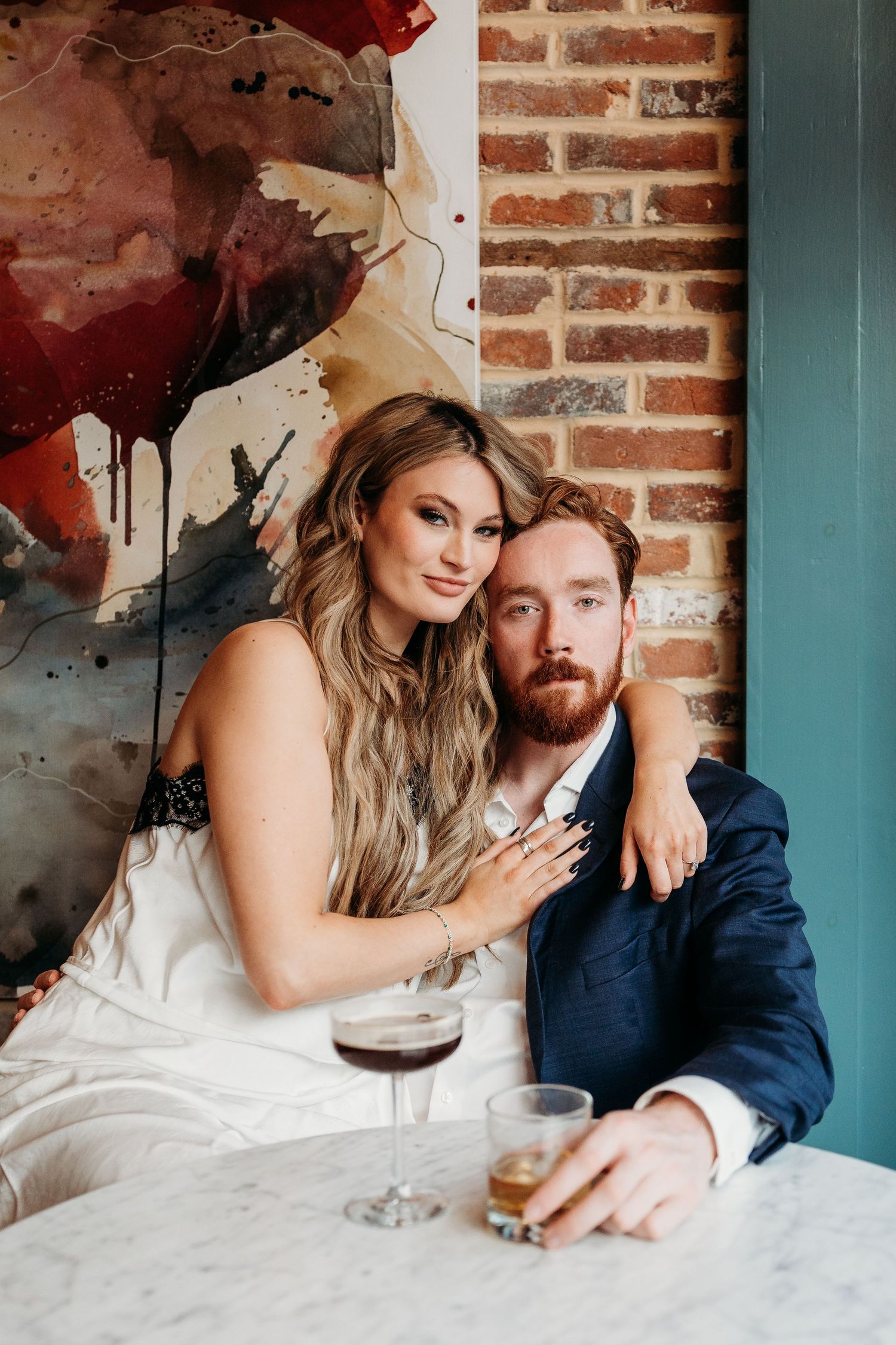 Couple shares intimate moments at a rustic bar with exposed brick wall and artistic red decor elements.