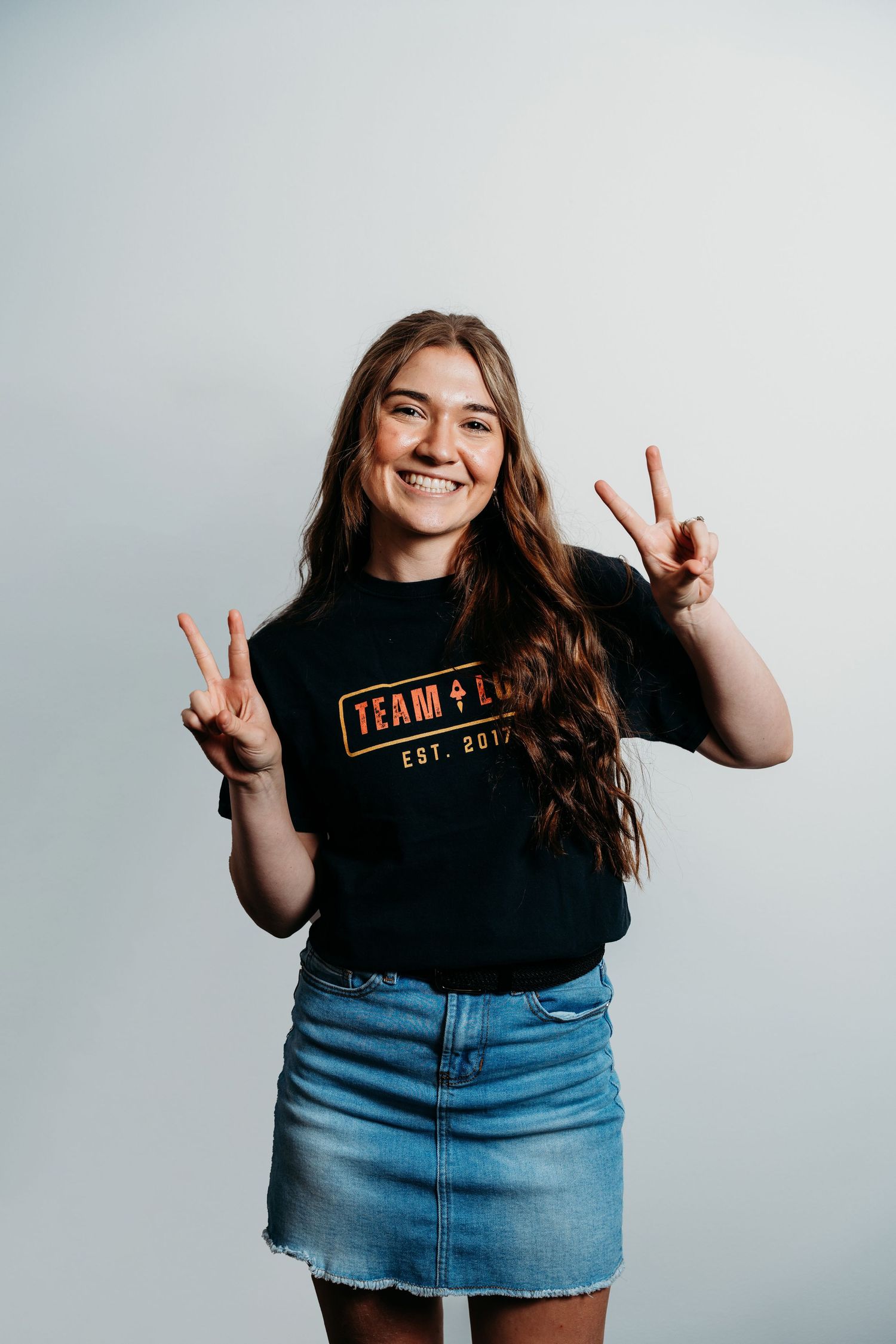 A person in casual denim showing peace signs against a plain white background.
