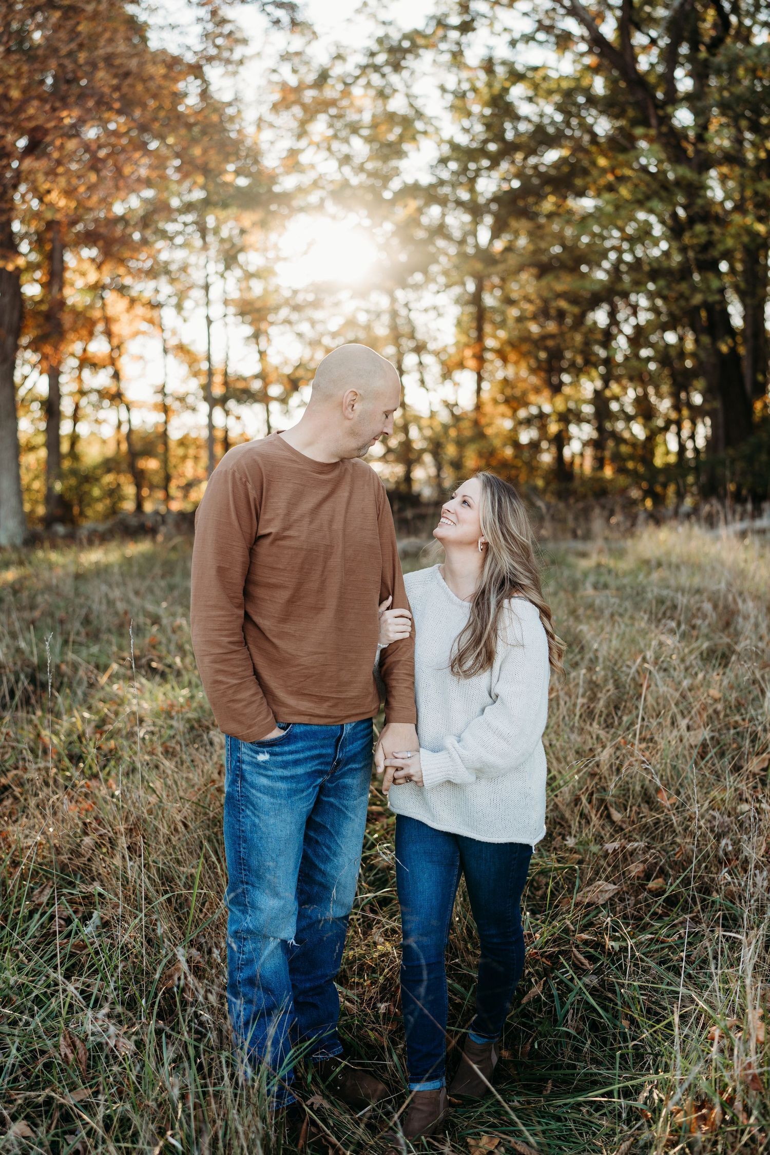 Couple sharing tender moment in sunlit autumn field with golden light filtering through trees.