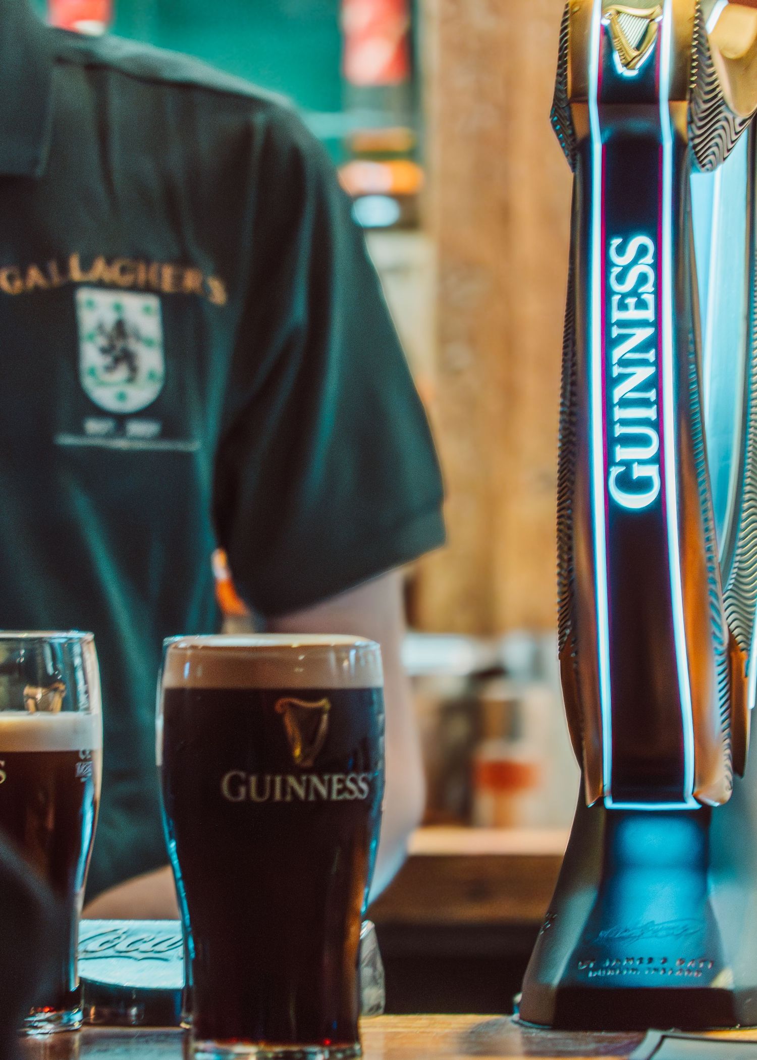 Several pints of dark Guinness beer sit on a bar counter with illuminated tap handles visible in the background.