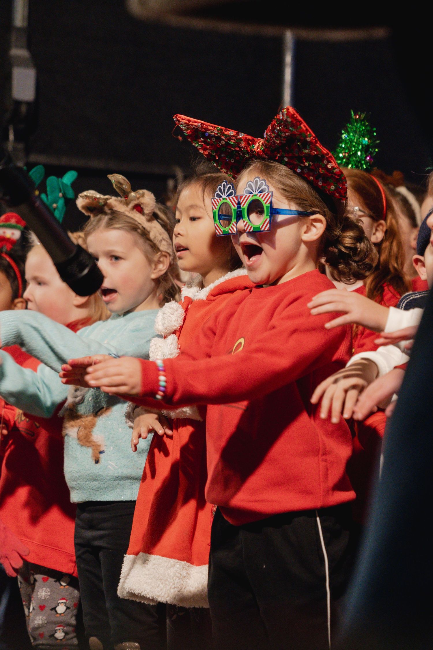 Children wearing festive holiday attire and sparkly decorations perform together during a Christmas celebration.