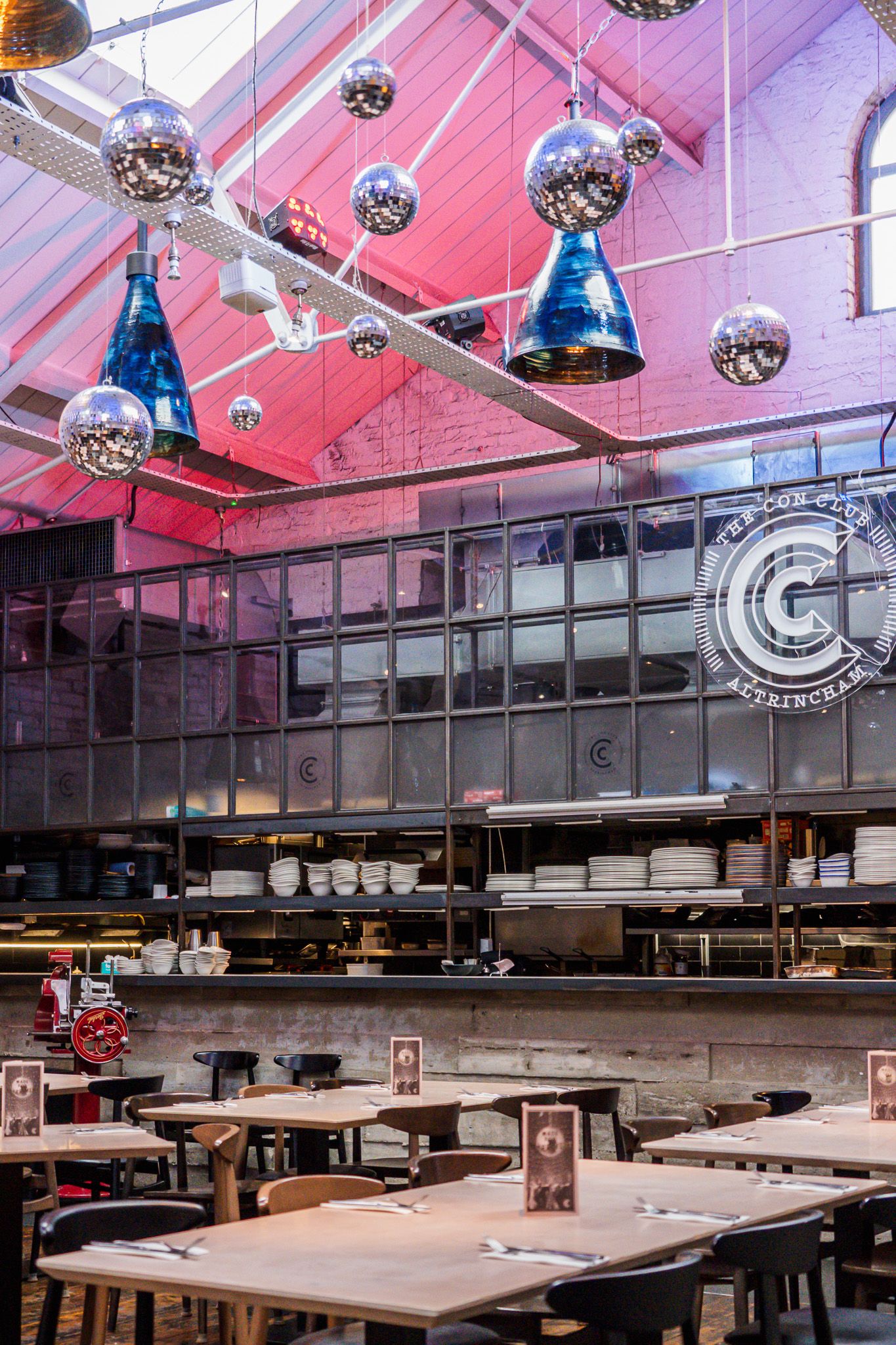 Modern restaurant interior with disco balls and industrial lighting fixtures above dining tables.