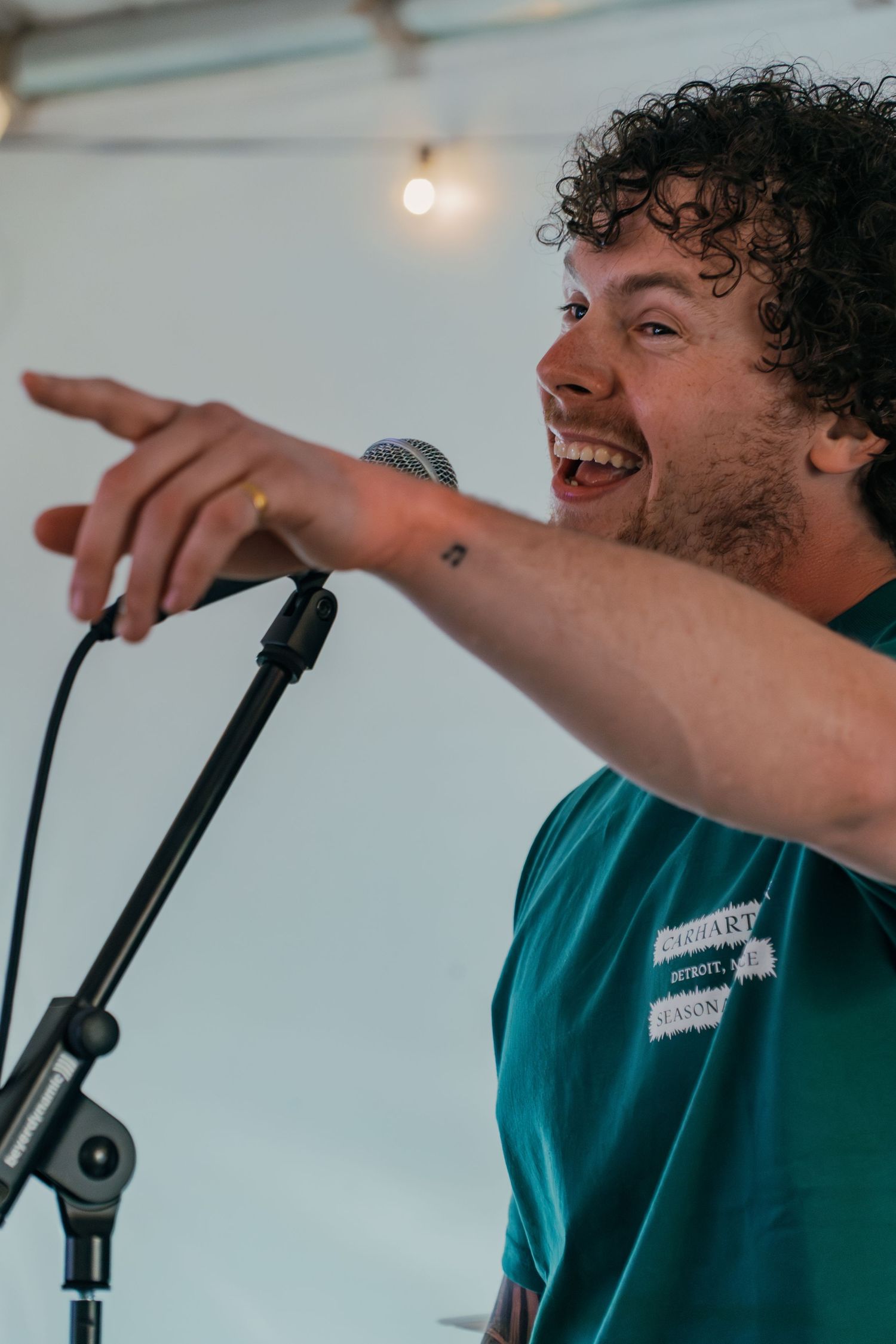 A performer in a teal shirt gestures enthusiastically while singing into a microphone during a live performance.