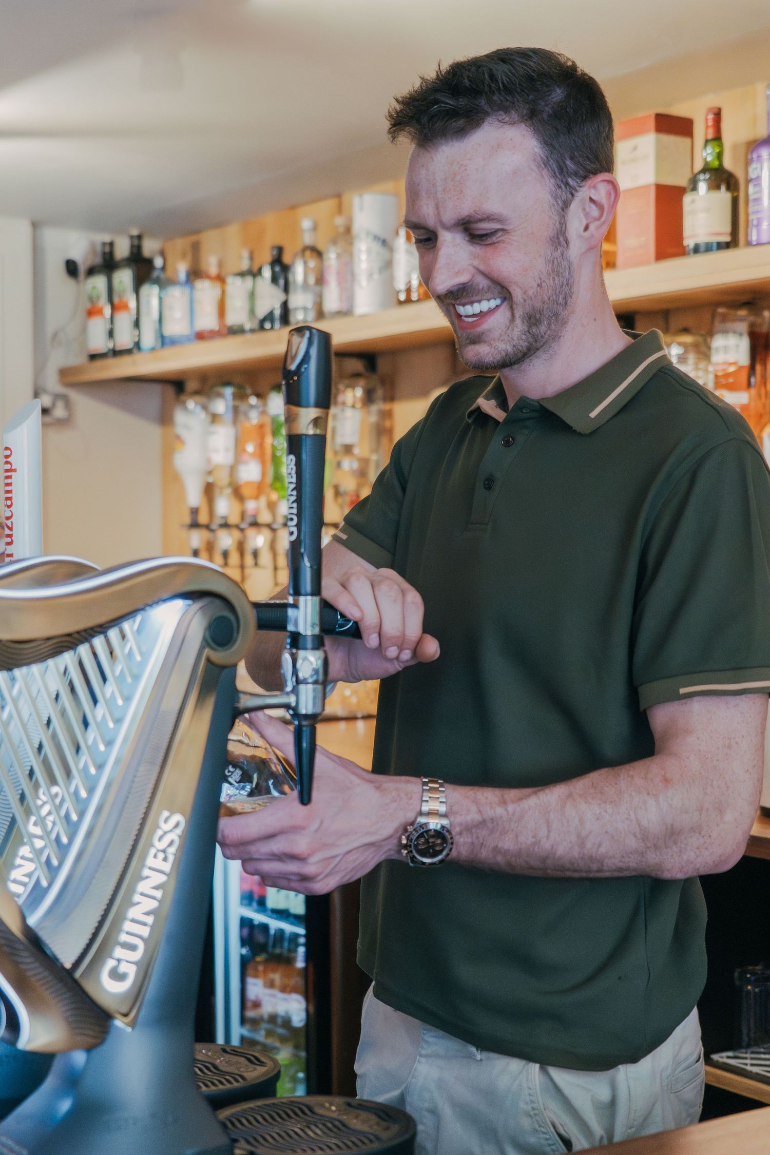 Bartender in green shirt pouring draft beer from tap system at bar counter.