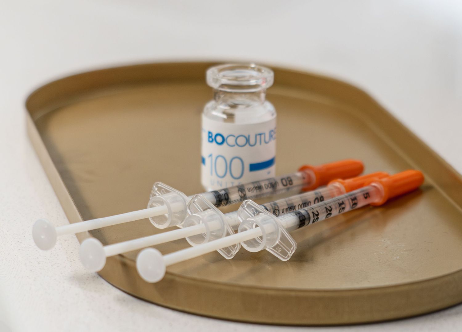 Bocouture 100 units vial with three insulin syringes on a beige tray for botulinum toxin injections.