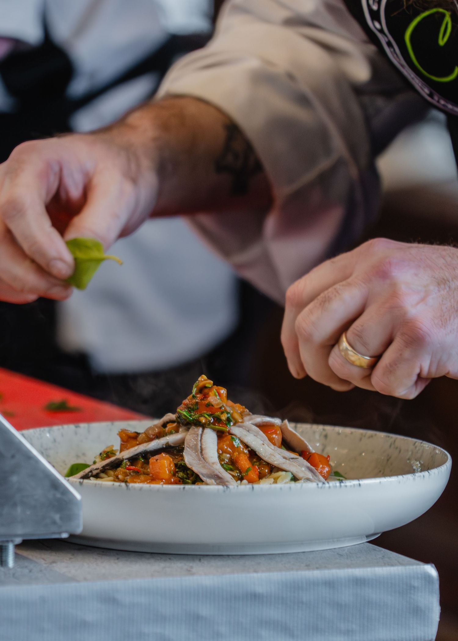 Chef plates an elegant dish with garnishes and sauces on a white plate in a professional kitchen setting.