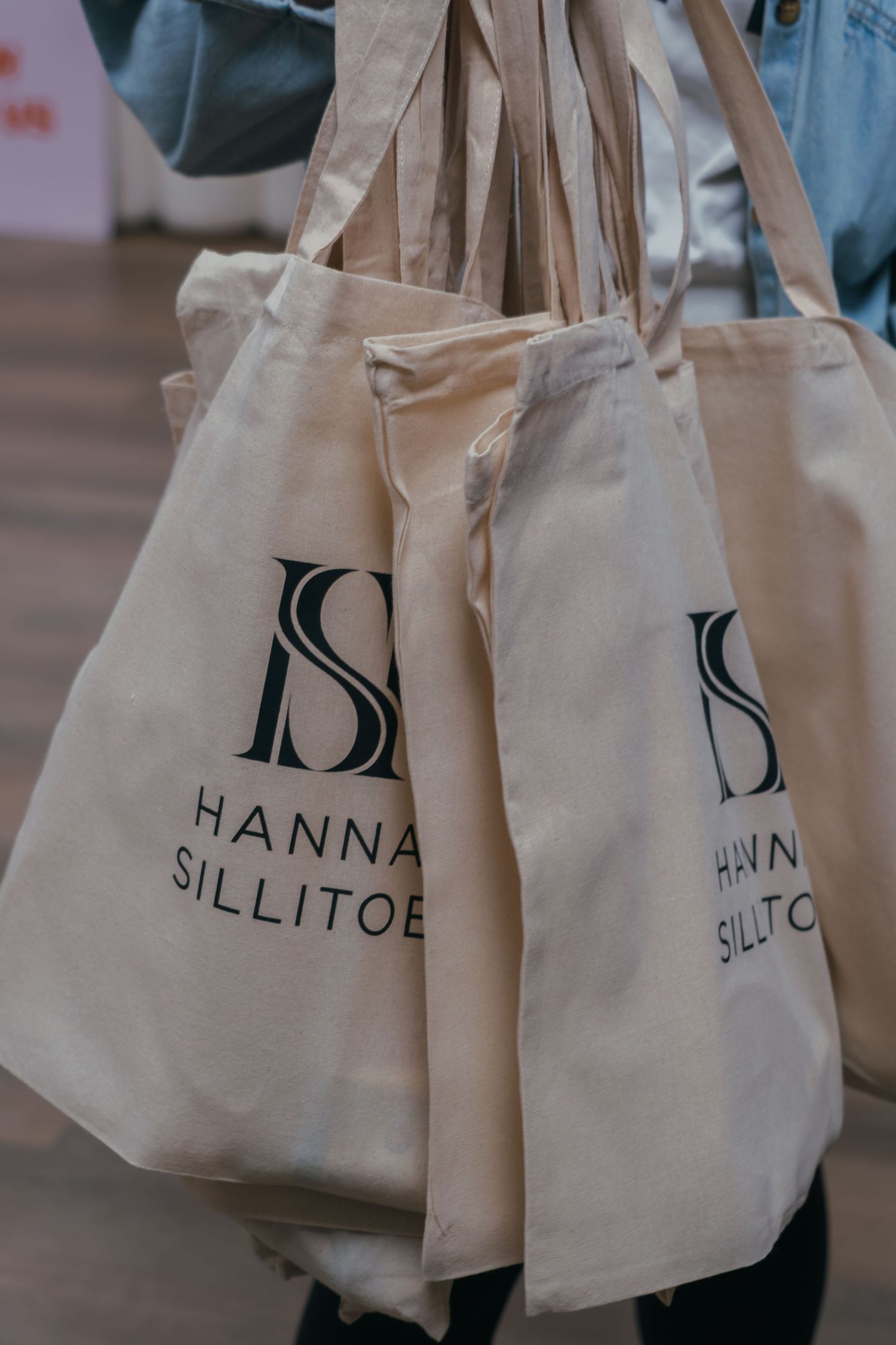 Multiple cream colored canvas tote bags with black text lettering arranged in a row on display.