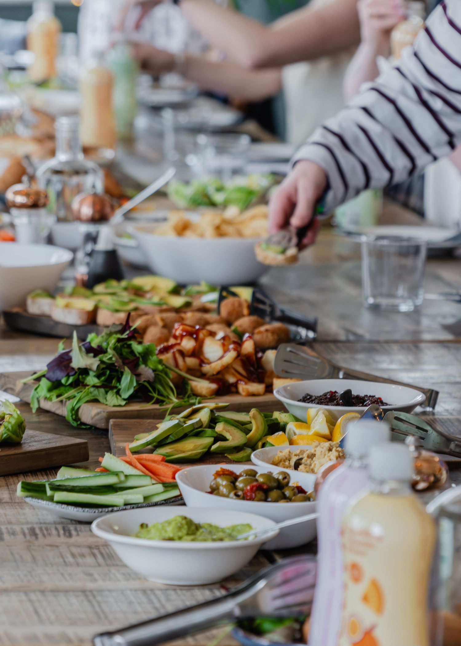 A vibrant spread of fresh vegetables, salads, and dips on a wooden table at a casual outdoor gathering.