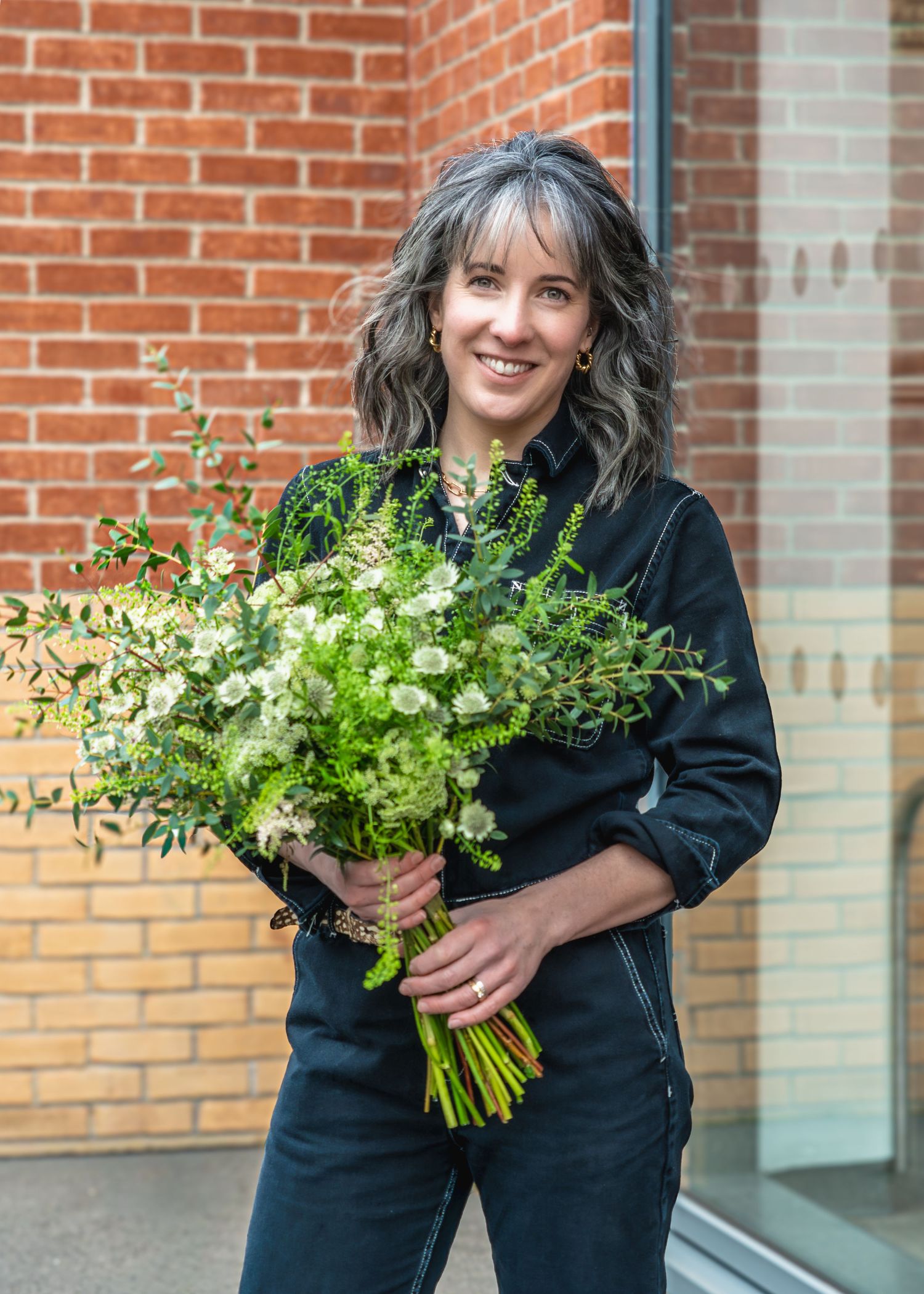 A person in black clothing holds fresh bunches of herbs against a brick wall background.