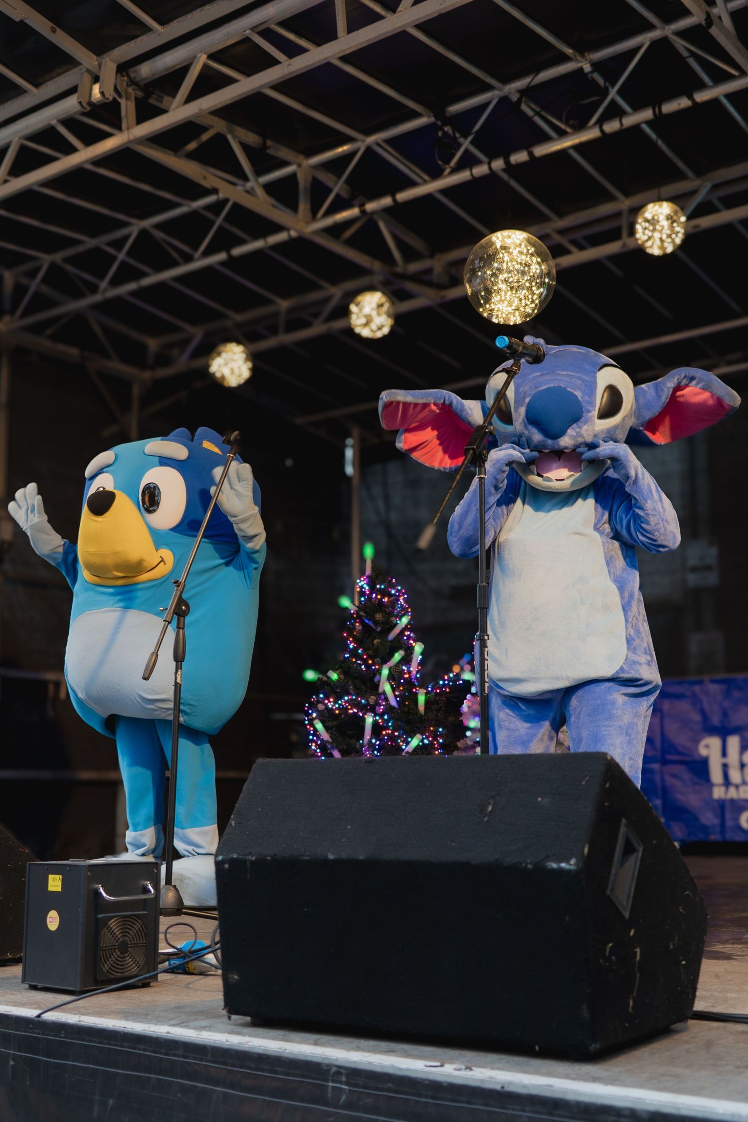Animated penguin mascot characters performing on a dark stage with illuminated spherical lights overhead.