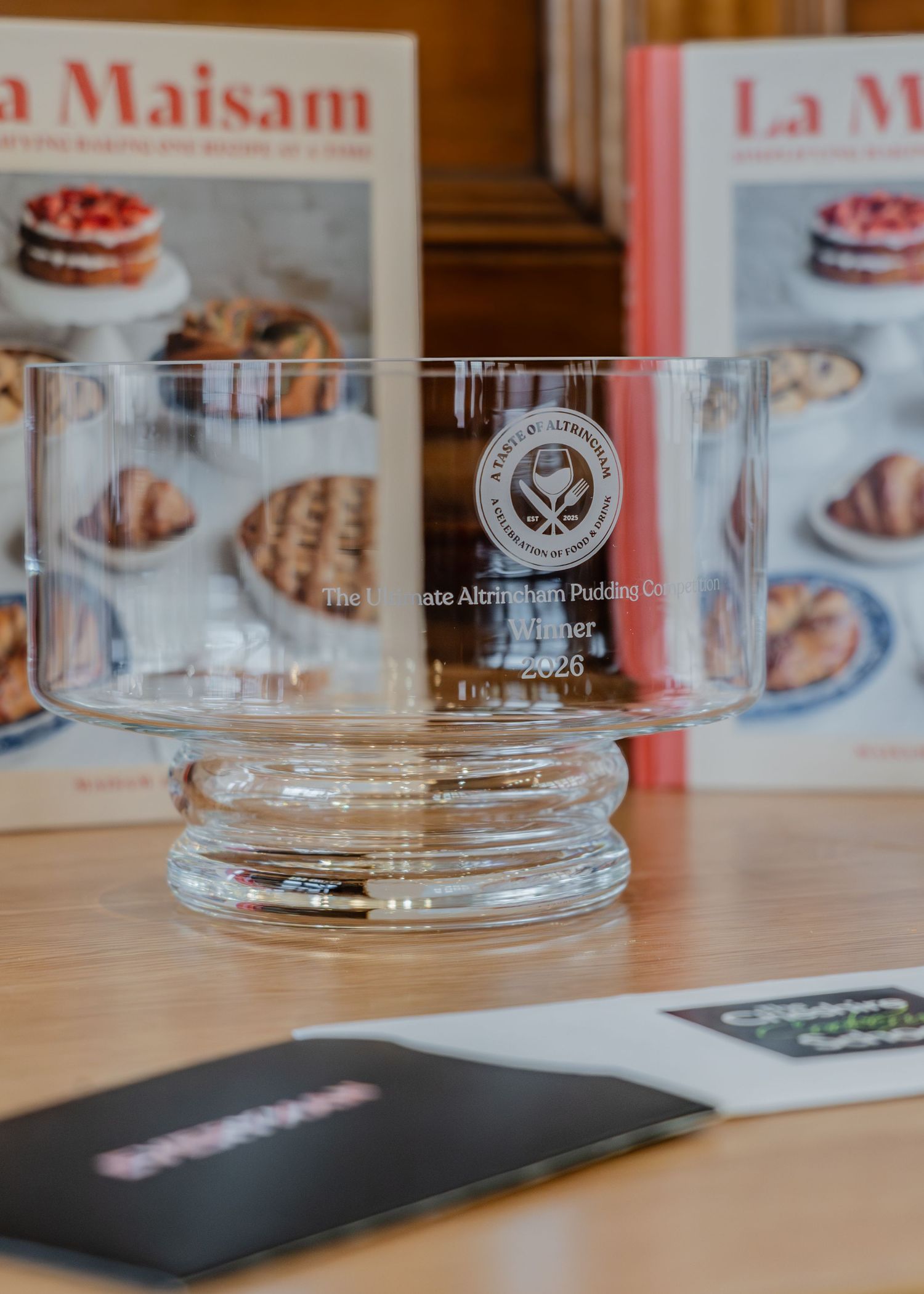 Clear glass tumblers lined up on a wooden surface with pink and white printed materials in the background.