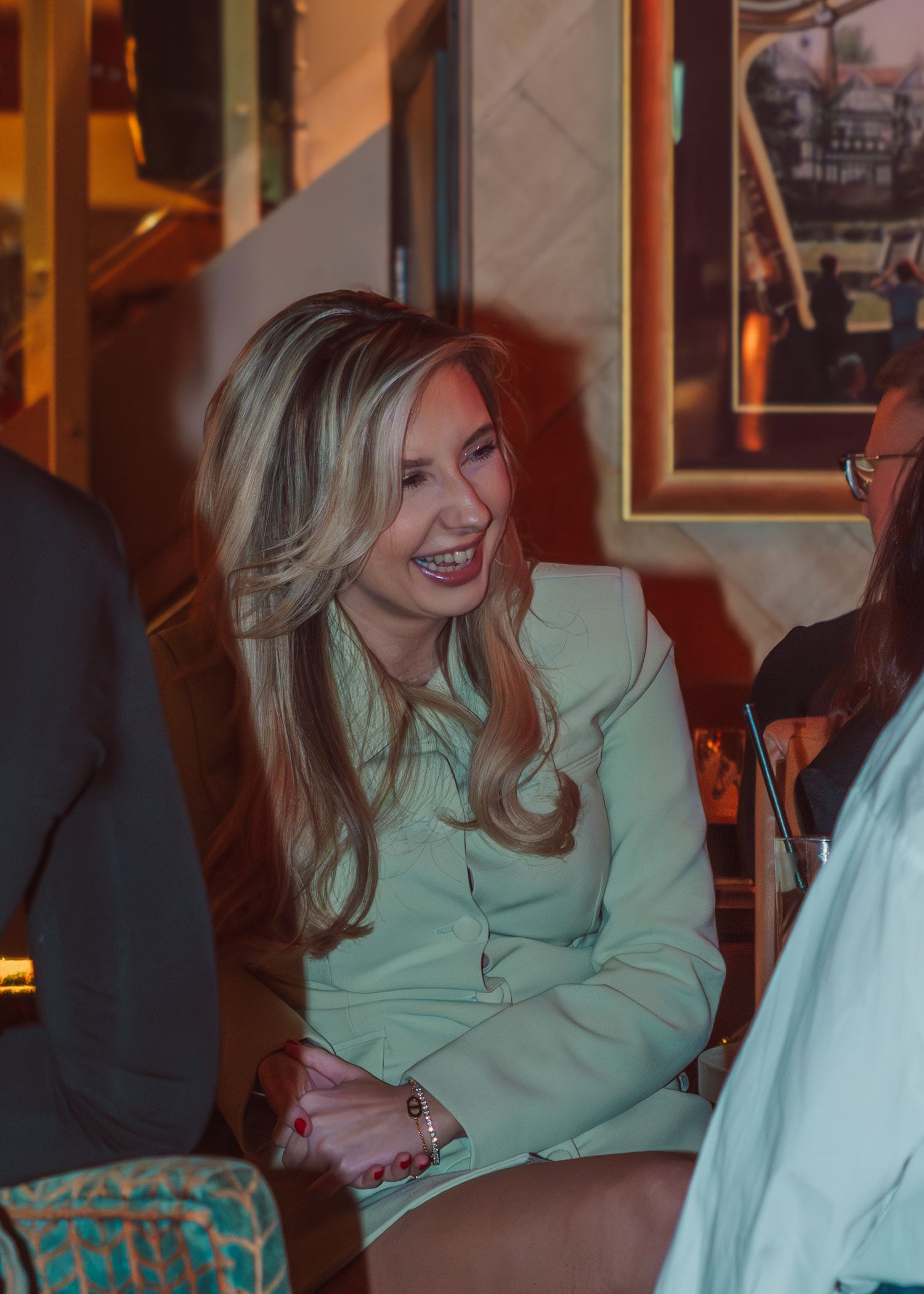A person in a mint green top smiles warmly while engaged in conversation at a restaurant setting.