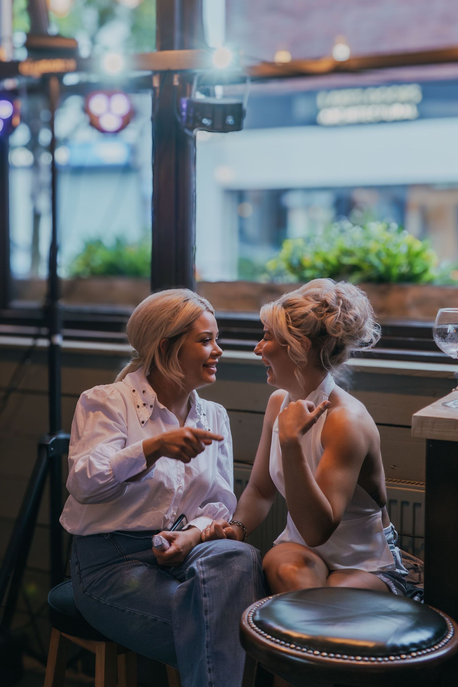 Two people share an intimate conversation while sitting at a restaurant table in moody lighting.