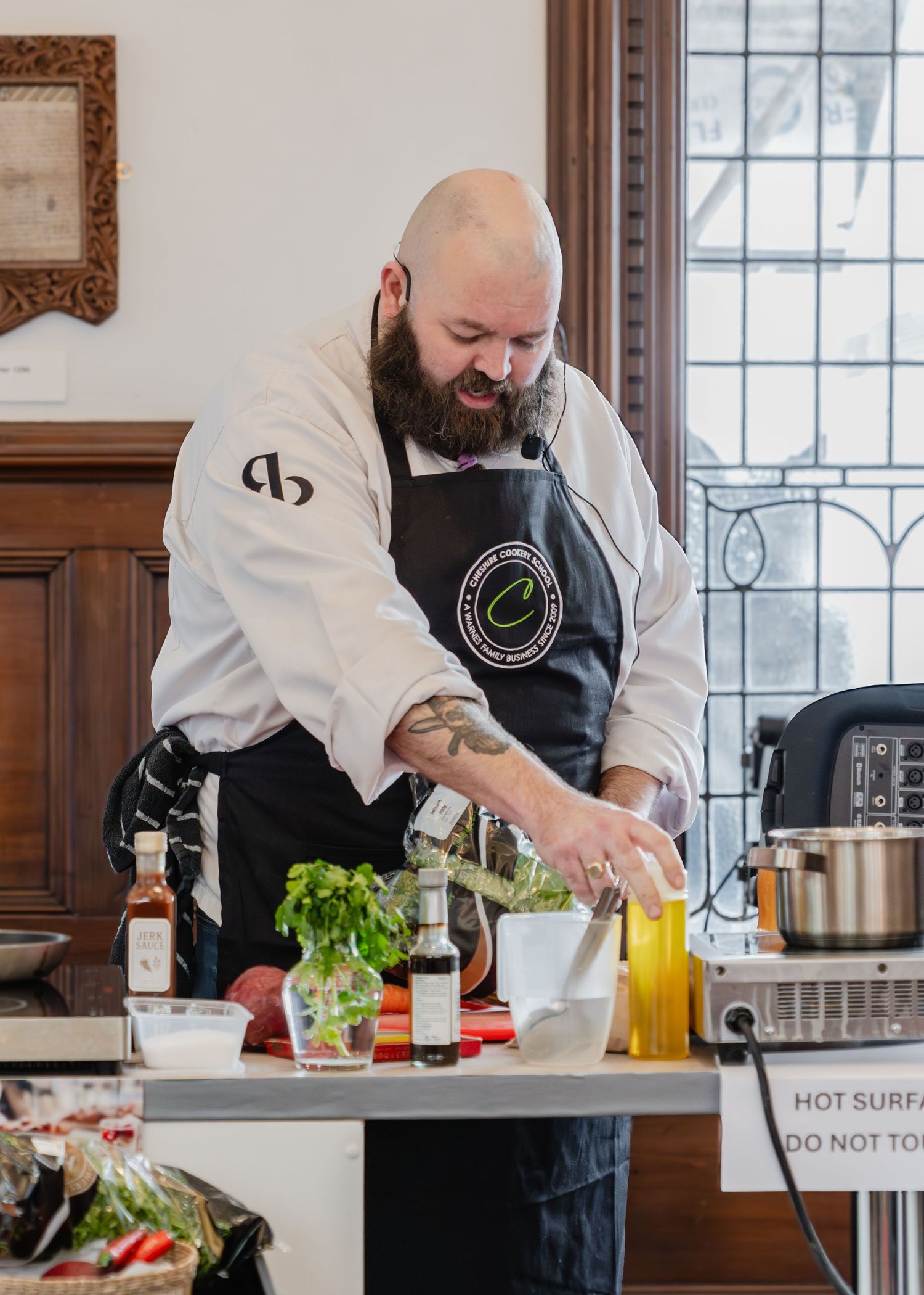 Chef in white coat preparing fresh ingredients and garnishes at a wooden bar counter with windows in background.