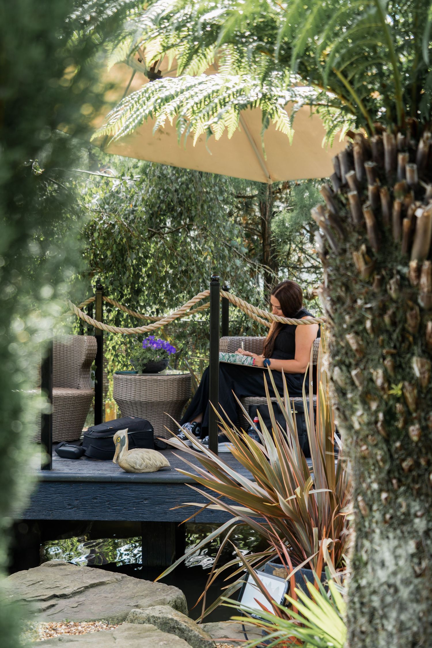 A serene outdoor lounge area with comfortable seating and umbrellas surrounded by lush garden foliage and trees.