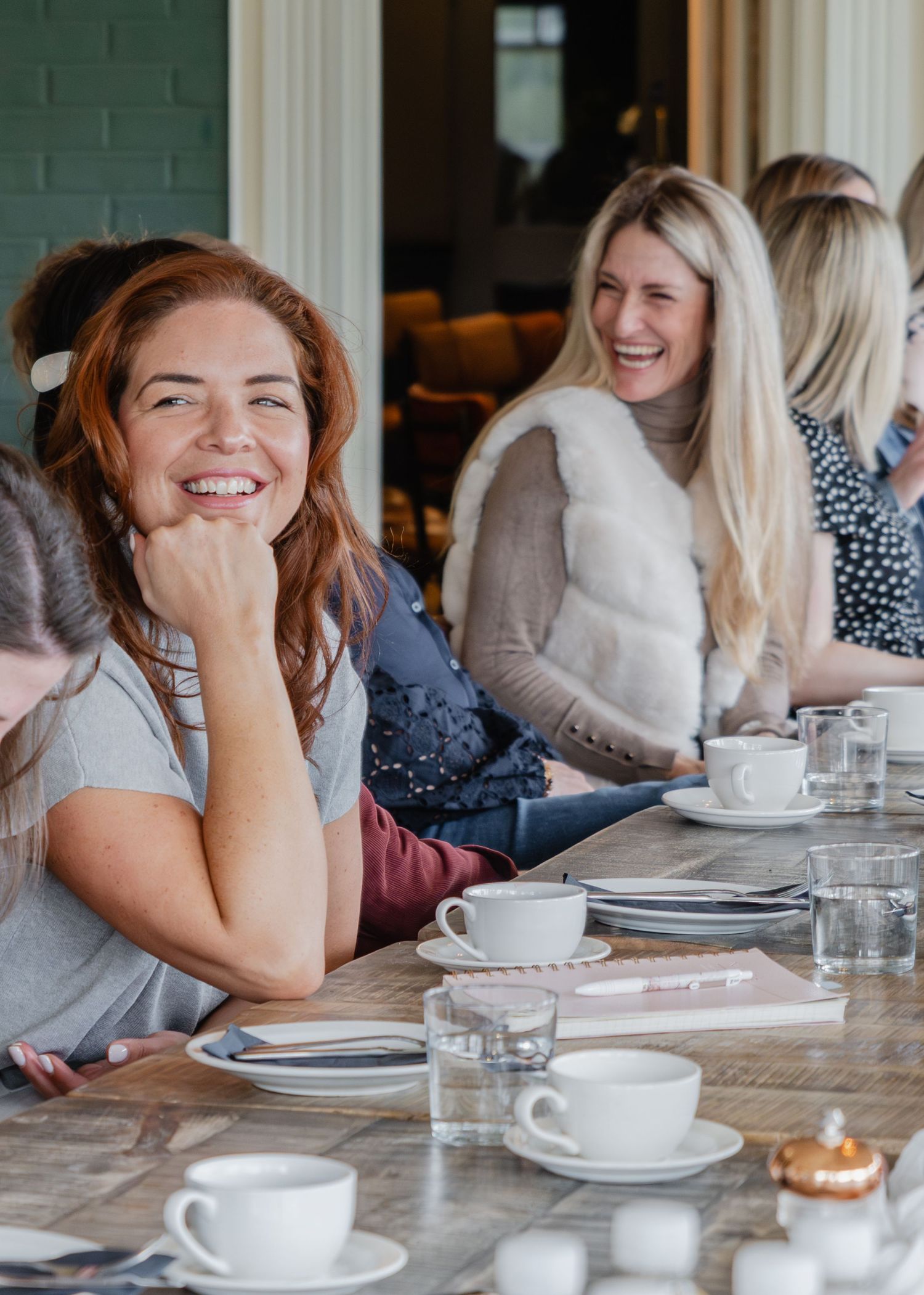 Women laughing and socializing at a restaurant table with coffee cups and water glasses.