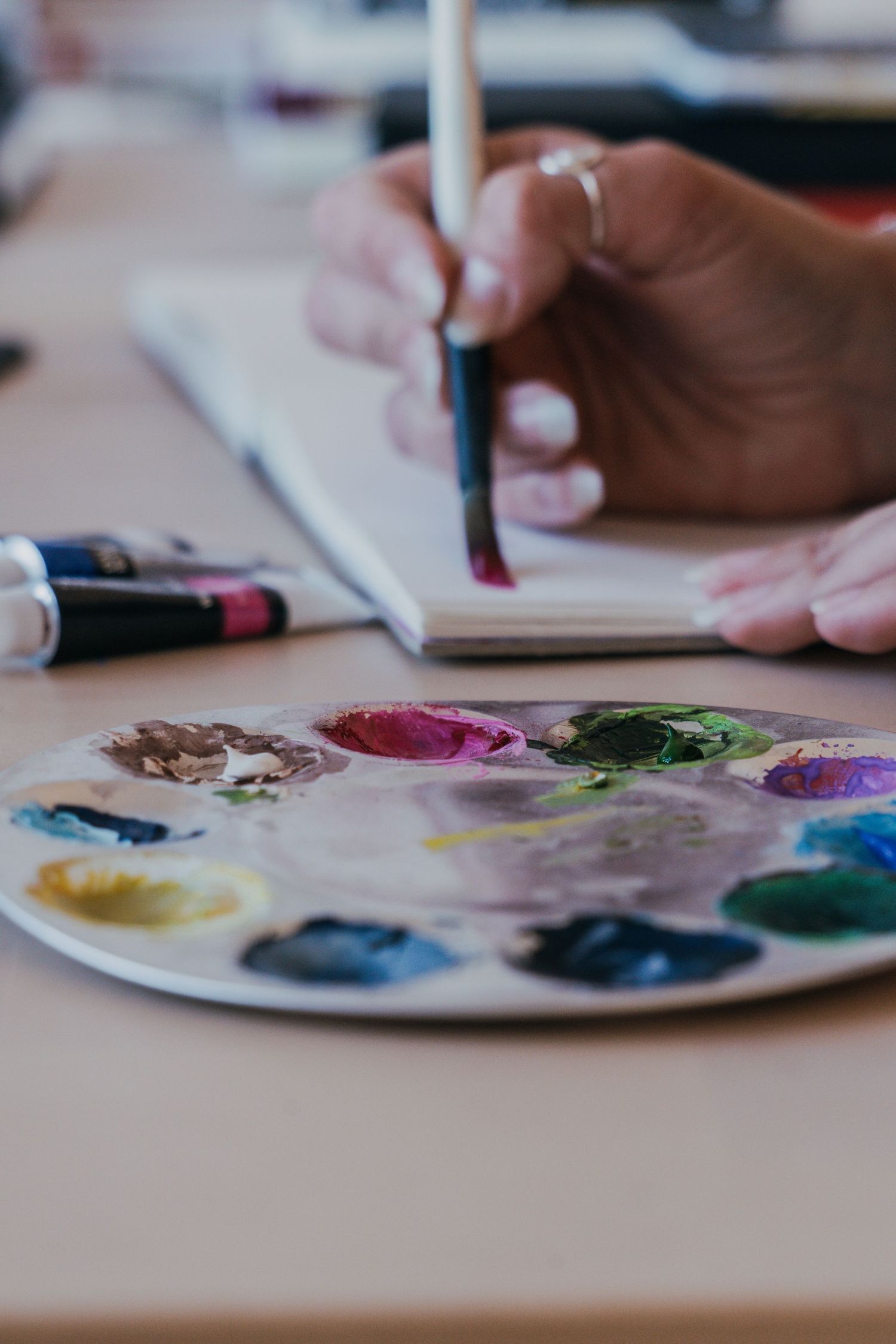 Artist's hands work with colorful watercolor paints on a white palette during creative painting session.