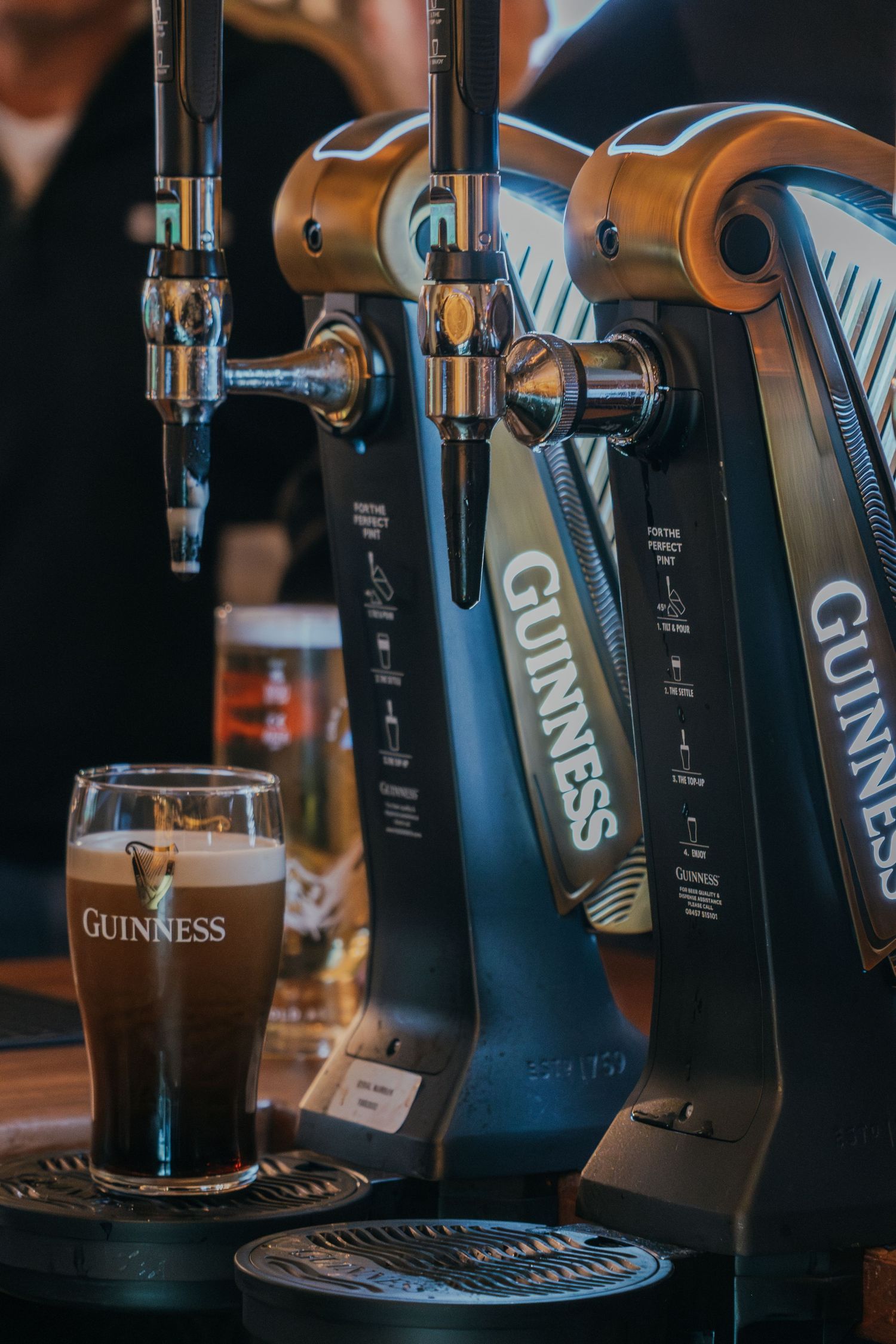 Multiple beer taps pouring dark Guinness stout into glasses at a bar with dramatic lighting.