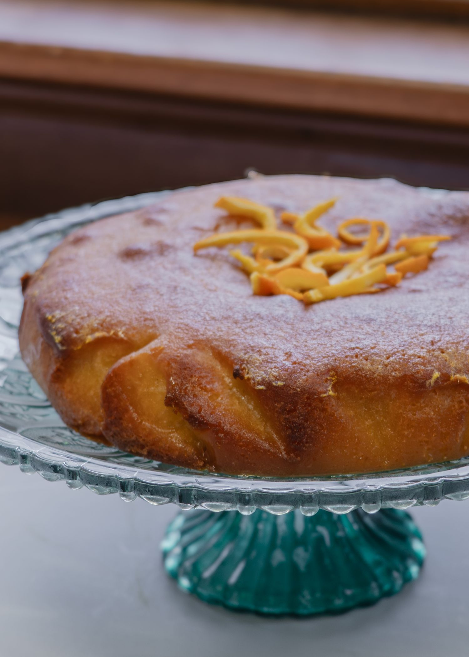 A homemade orange cake on a teal glass cake stand photographed in a progression of slices being removed.