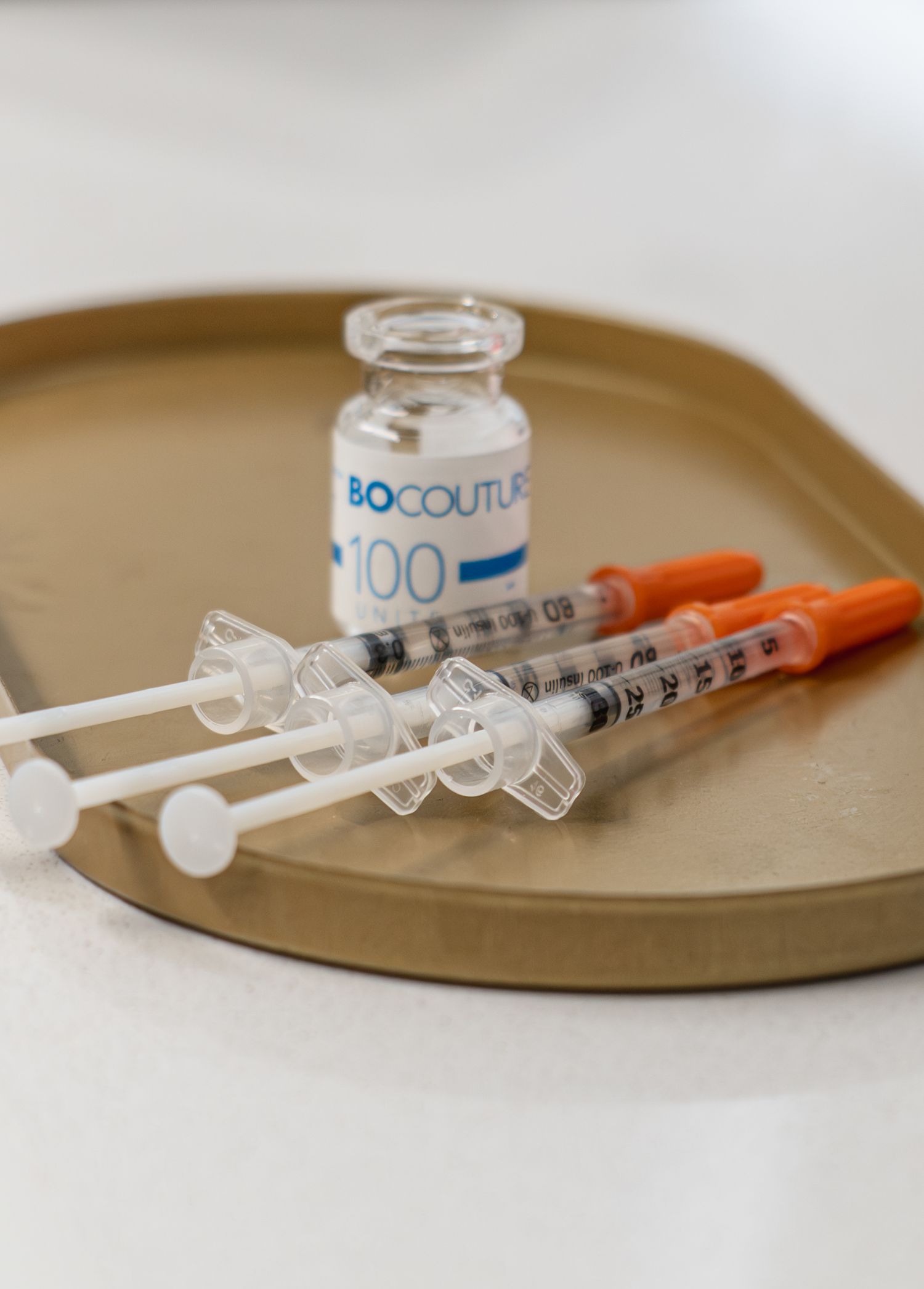 Medical syringes and vials arranged on a beige surface showing progression of injection preparation steps.