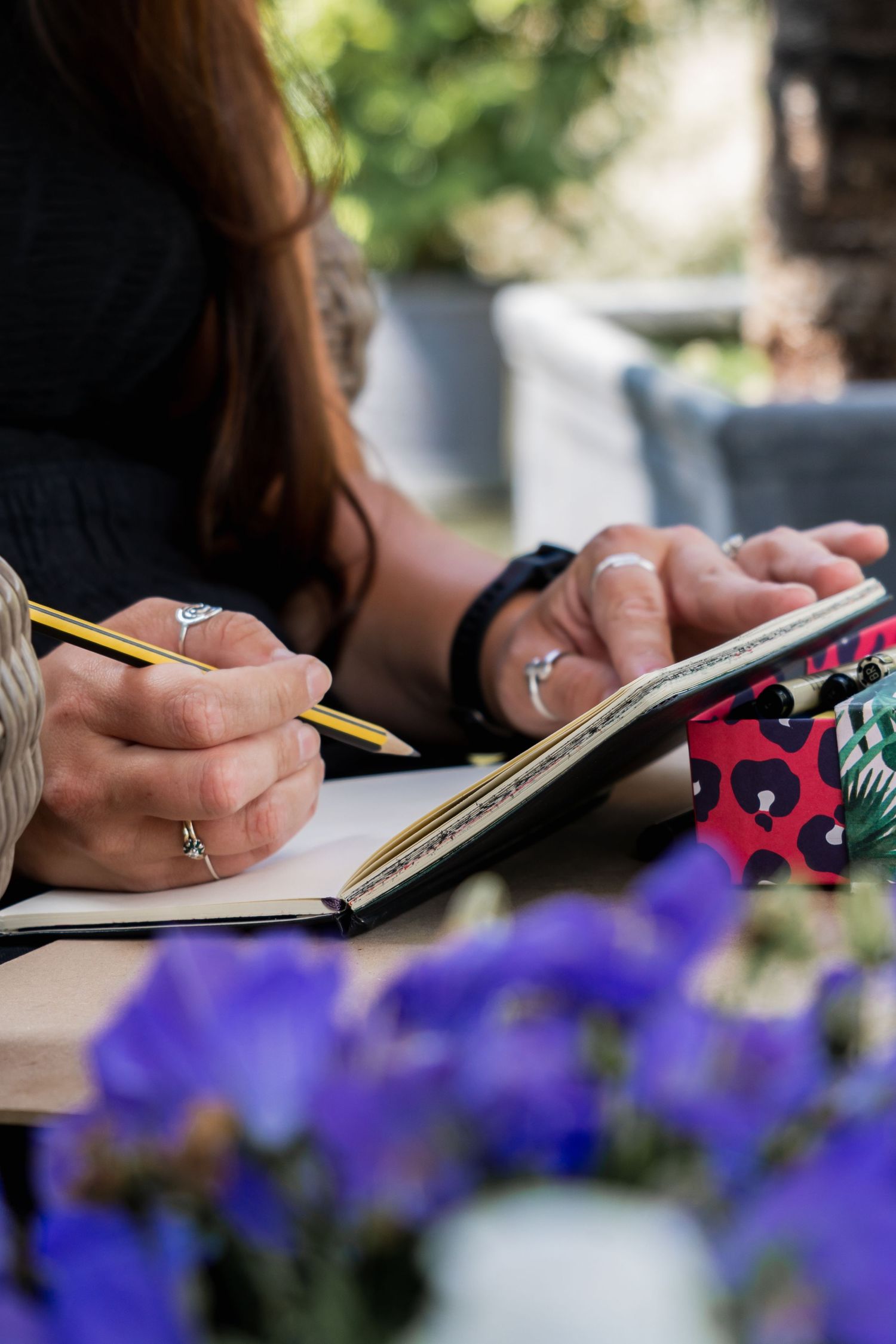 Someone writes in a journal outdoors with purple flowers in soft focus in the foreground.