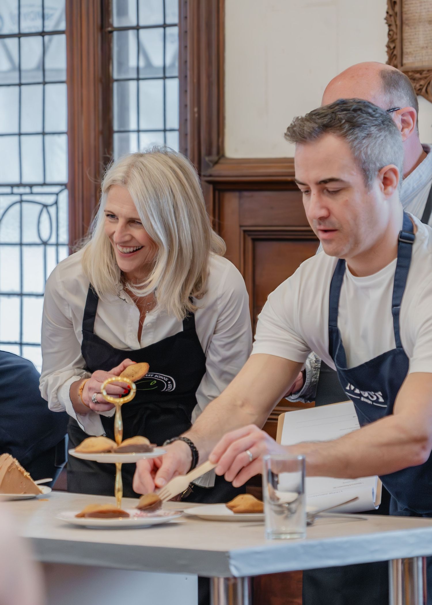 Group of chefs in aprons leaning over a counter while examining and discussing food items.