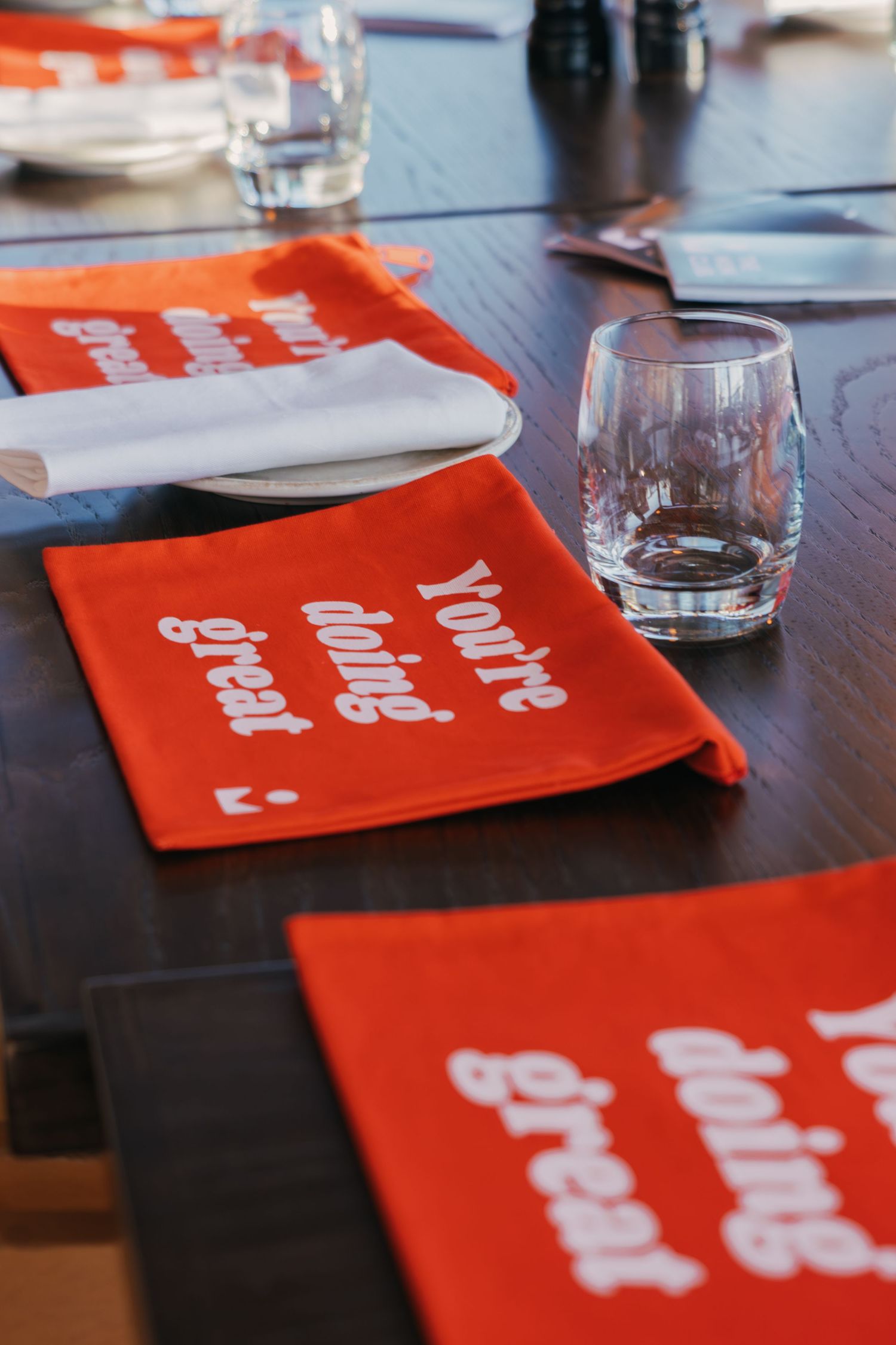 Red paper napkins with white text arranged on a dark wooden table with water glasses in the background.