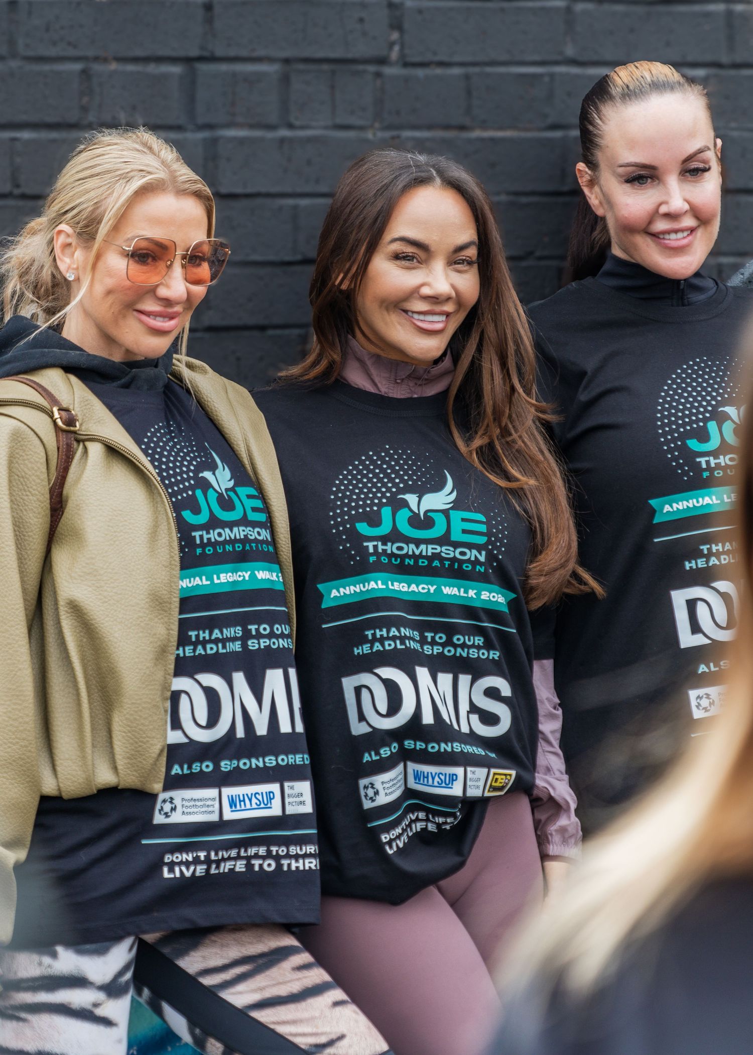 Three women smiling outdoors wearing Joe Thompson Foundation Annual Legacy Walk sponsor t-shirts.