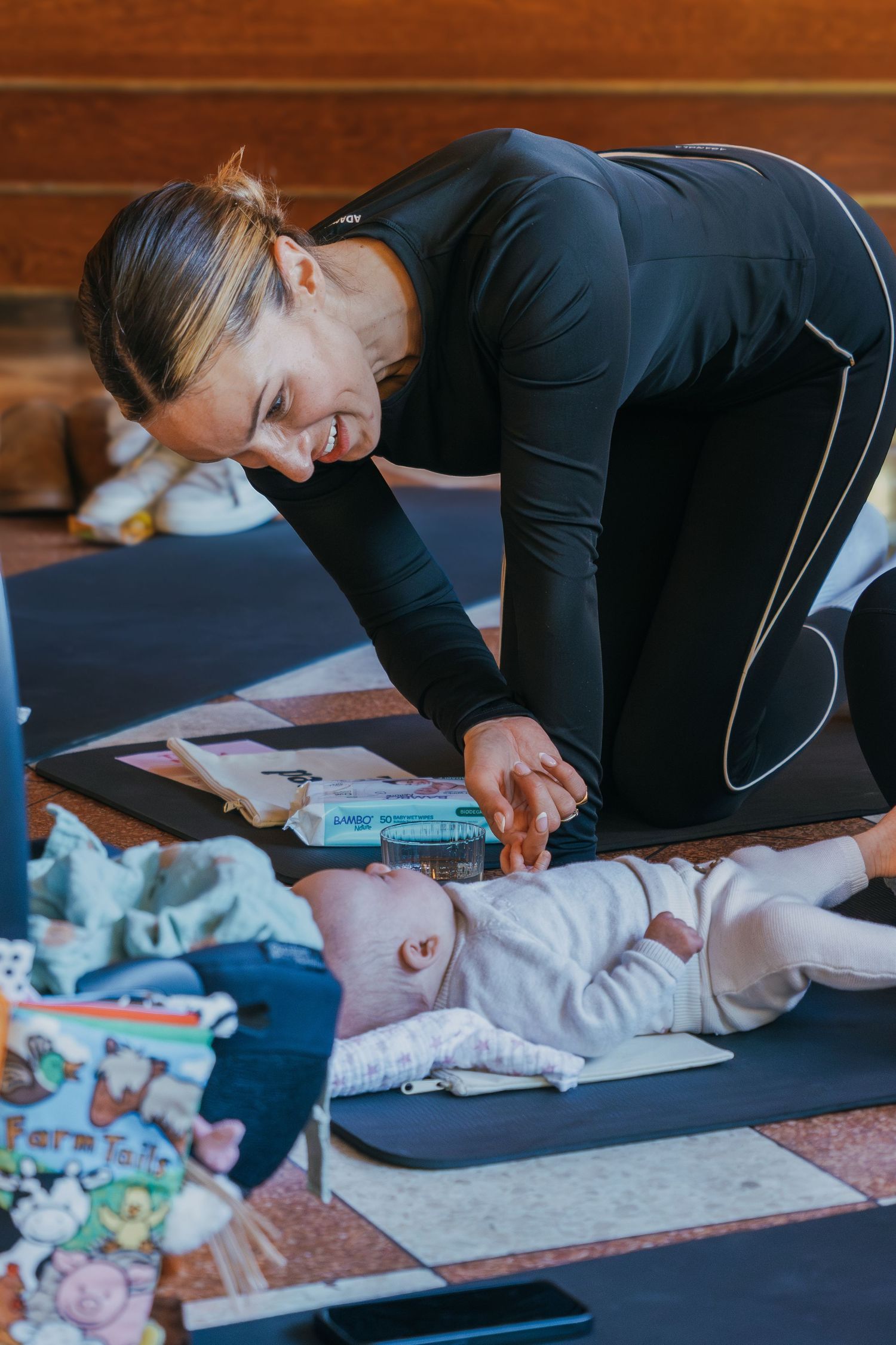 A person in black athletic wear practices baby massage techniques on a soft mat during an infant care class.