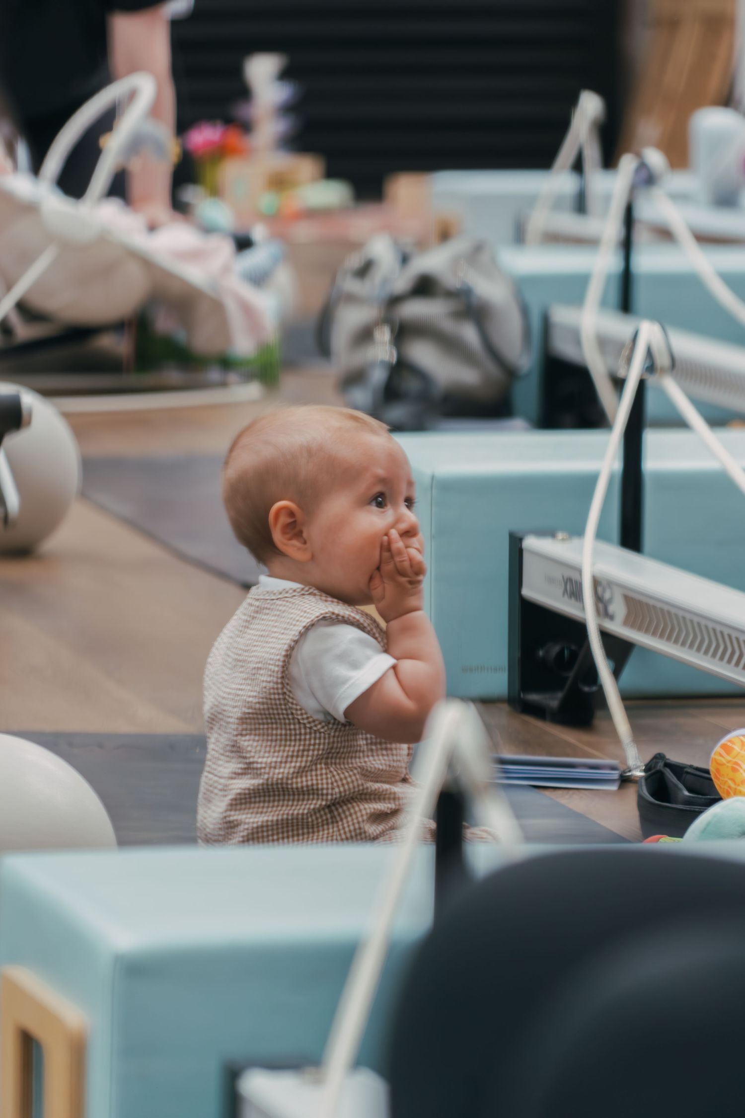A baby in a light colored shirt sits at a desk in an office environment, looking upward with curiosity.