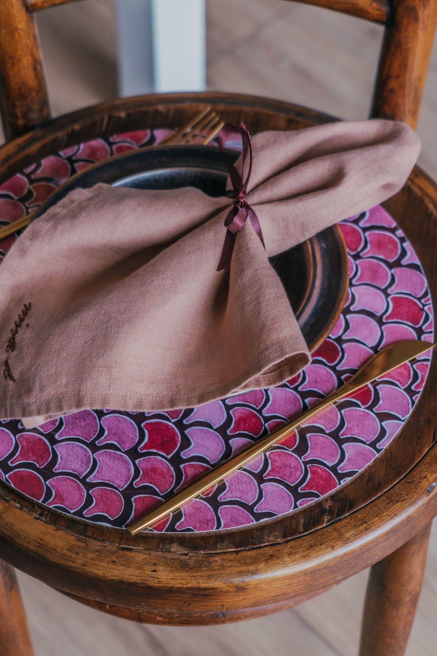 A pink and purple mermaid scale patterned fabric is draped over an antique wooden chair seat.