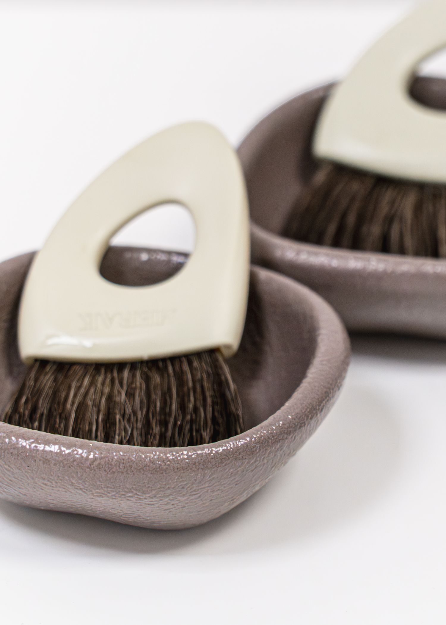 Two brown ceramic dishes with cream-handled dark bristle brushes, elegant grooming tools on white background.