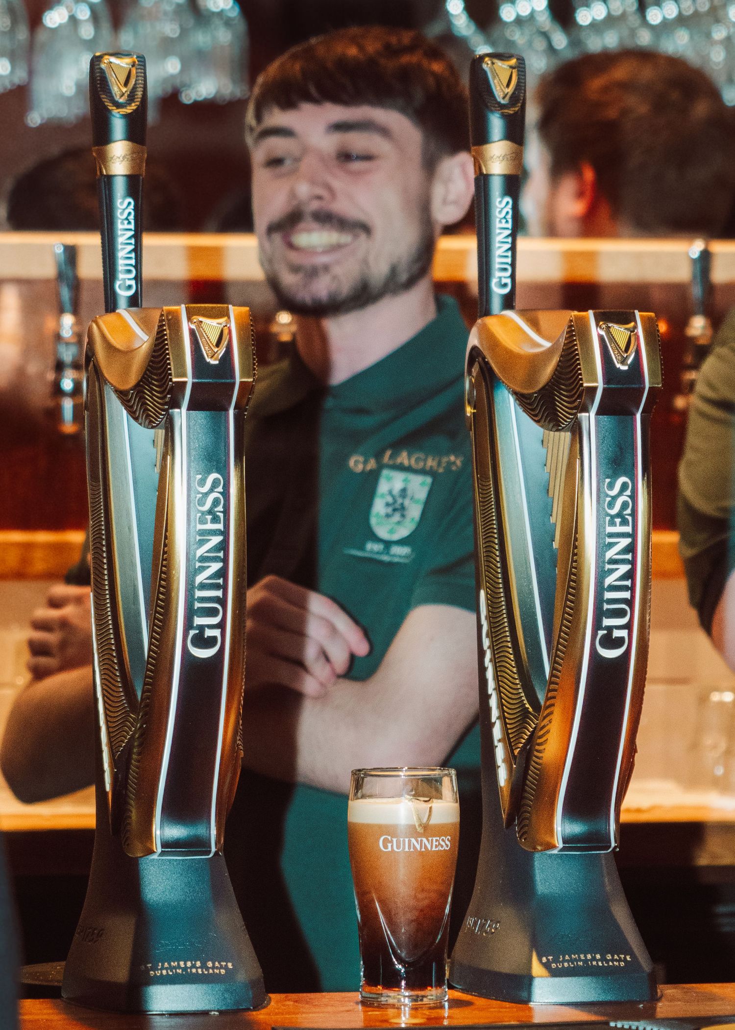 Guinness beer taps and glasses lined up at a bar counter with warm lighting and wooden decor.