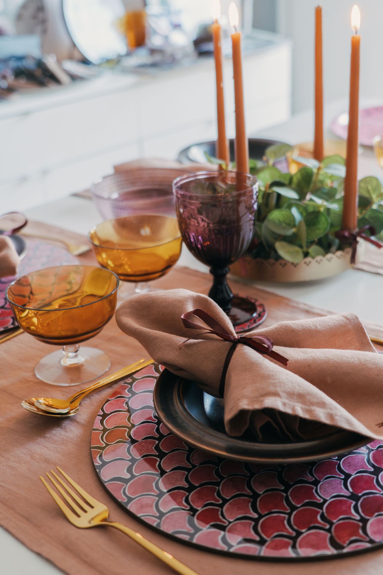 Elegant table setting with copper tones featuring scalloped placemats, amber glassware, and brown plates with orange candles.
