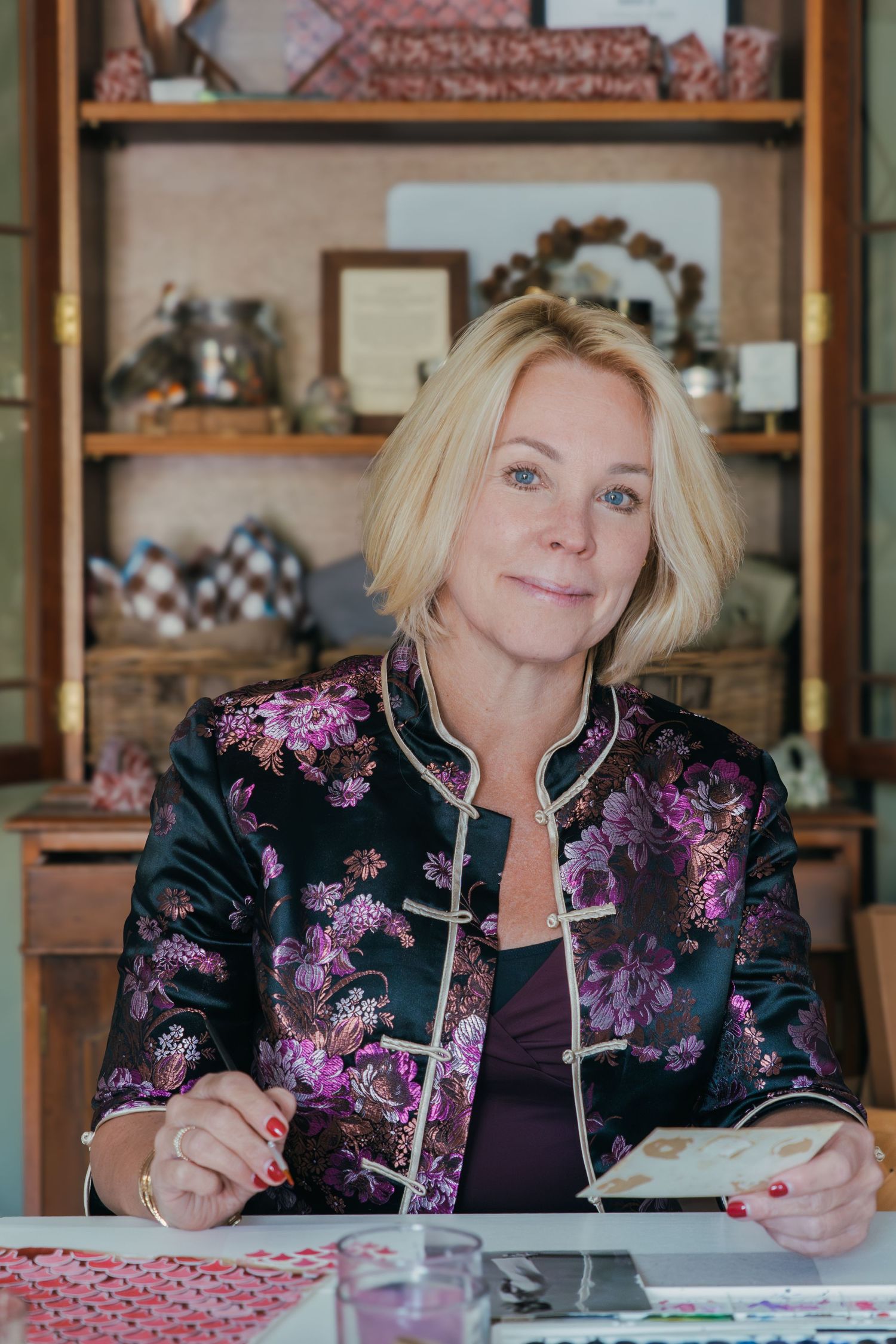 A person in a floral jacket sits at a table writing in a notebook in a cozy indoor setting.