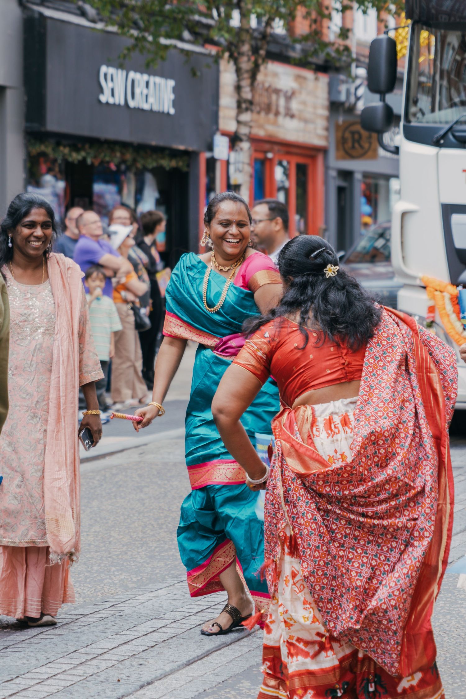 A group in colorful traditional South Asian attire dancing and celebrating together on a city street.