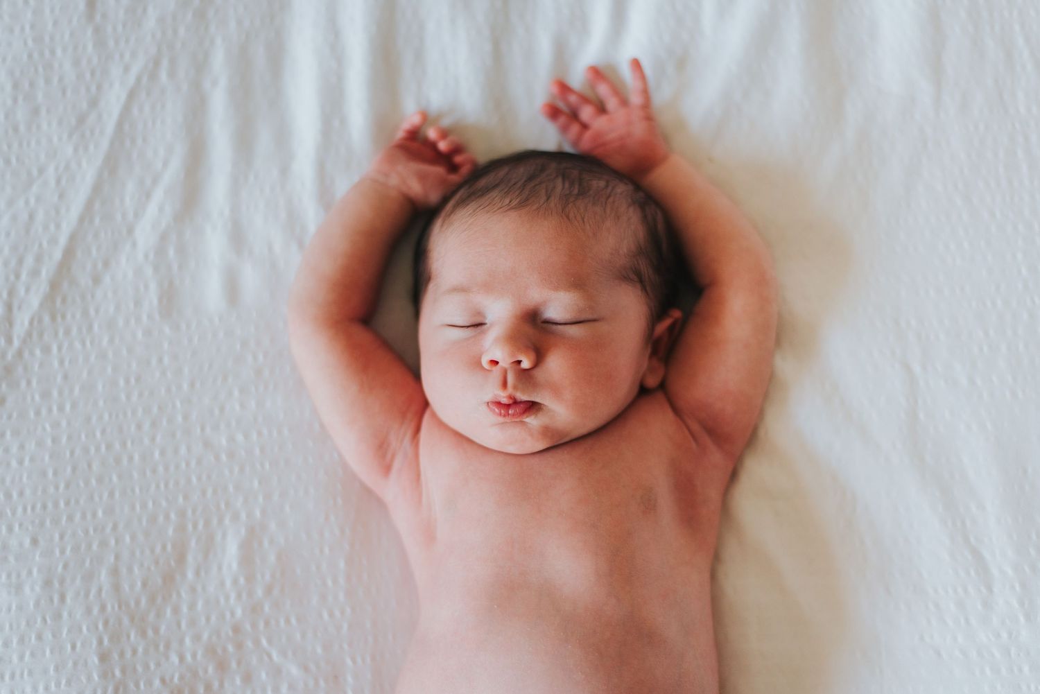 Baby lays on bed with arms over head