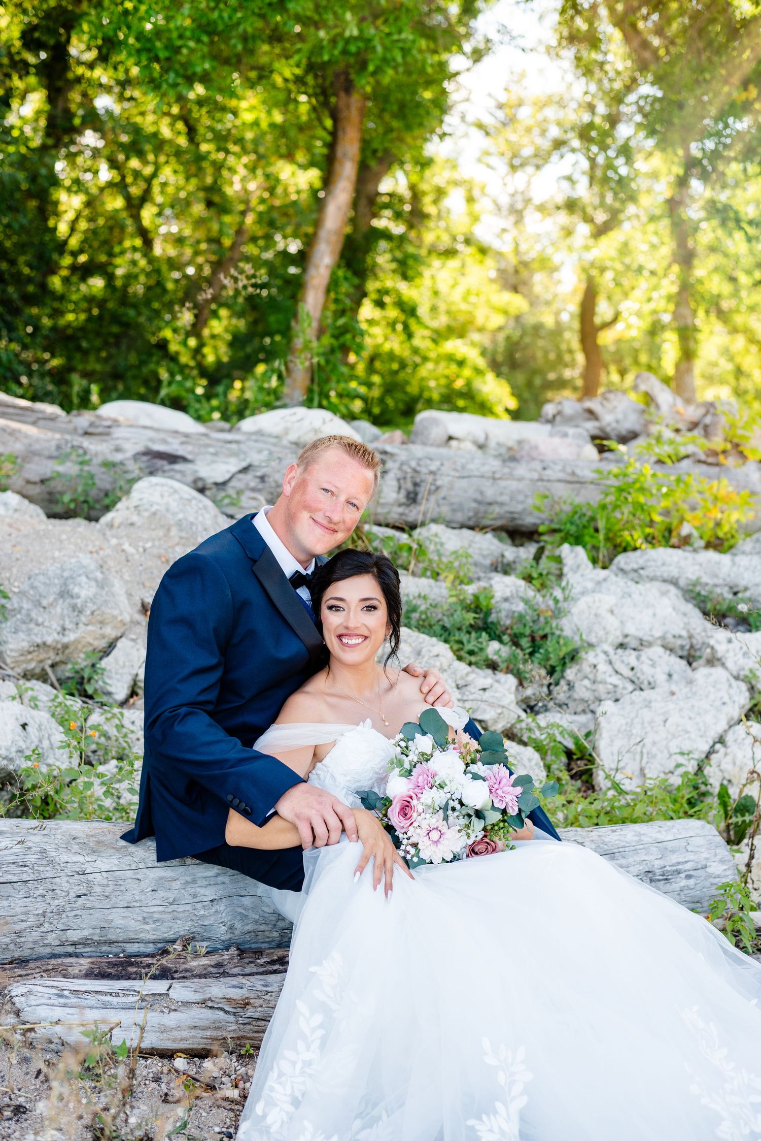Couple sits on rocks on wedding day