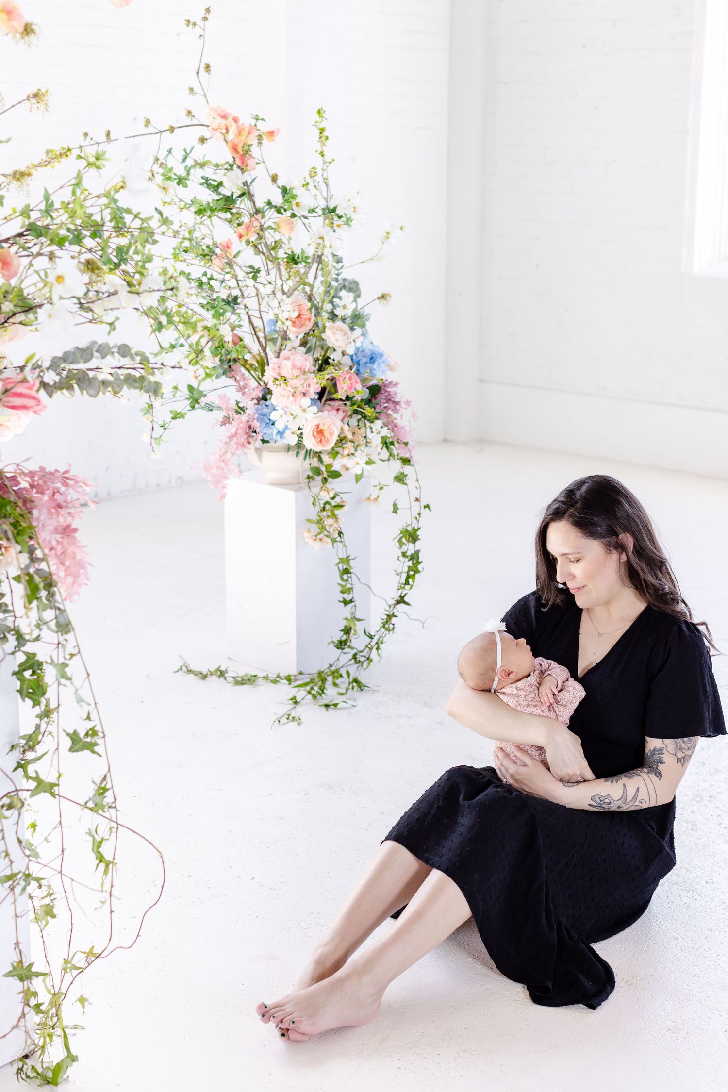 Mother wearing black dress with ling dark brown hair holding baby in pink clothes, in professional photo studio in Winnipeg for mothers  day