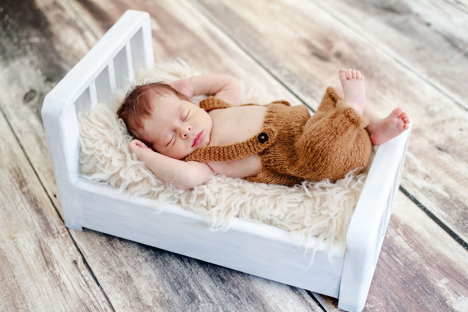 Baby lays with hands behind head on little bed