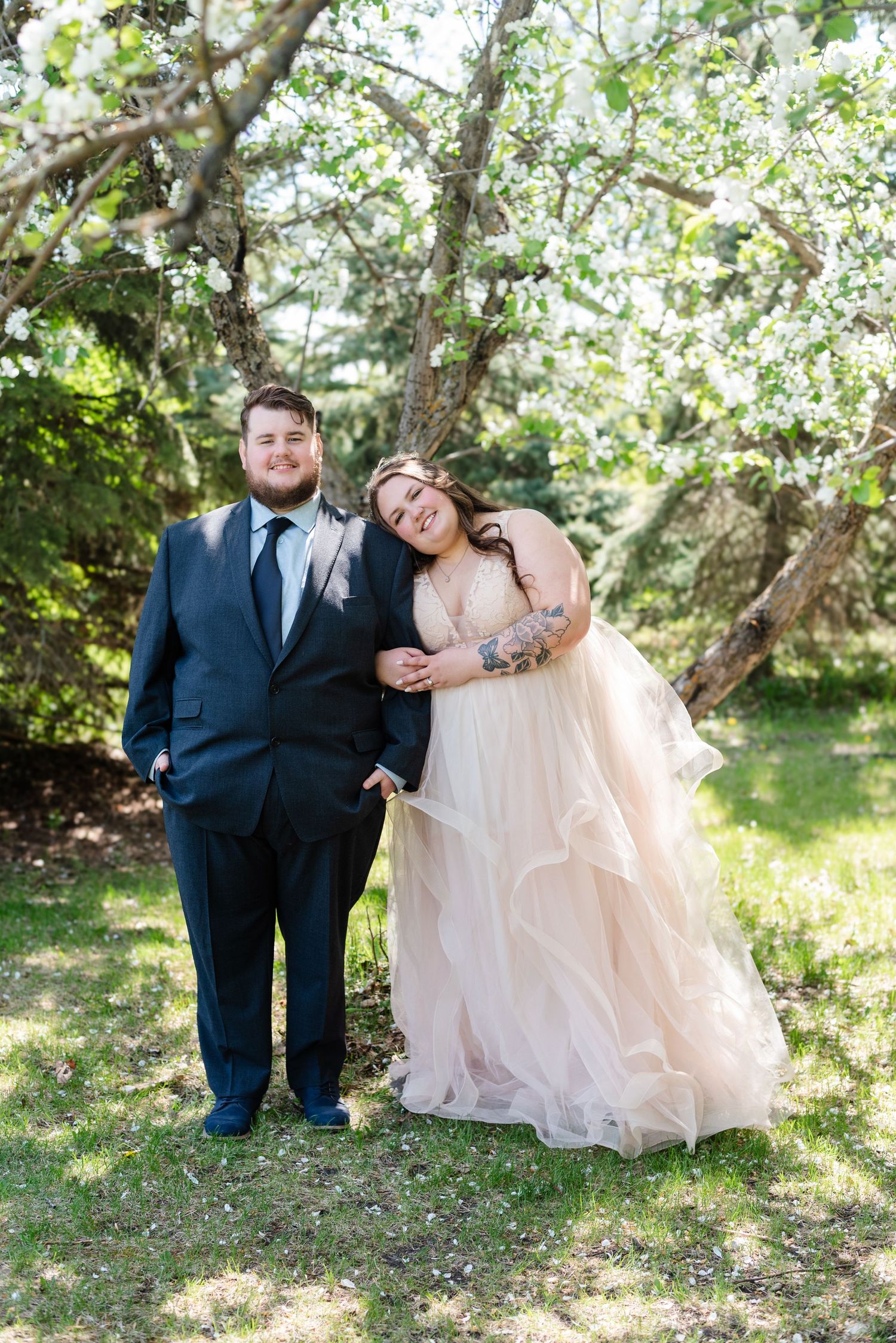bride and groom pose under blossom tree after wedding