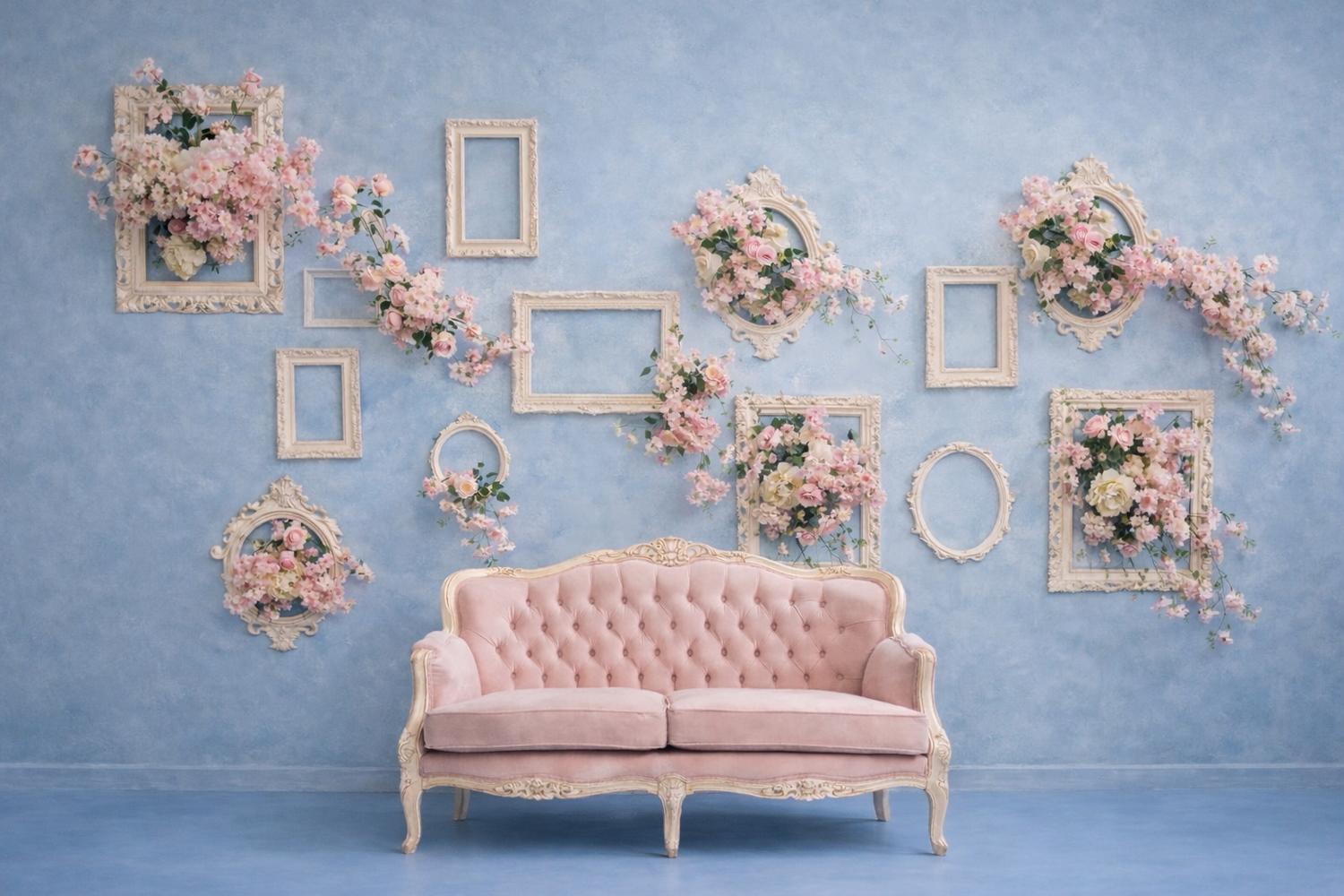 Pink vintage couch against blue wall, with cream picture frames on walll behind, with flowers in the frames.