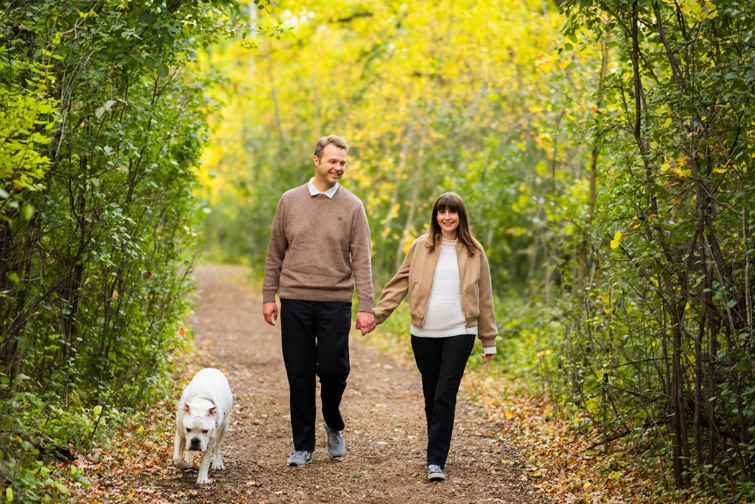 Couple walks their dog in a park during fall in winnipeg during photoshoot