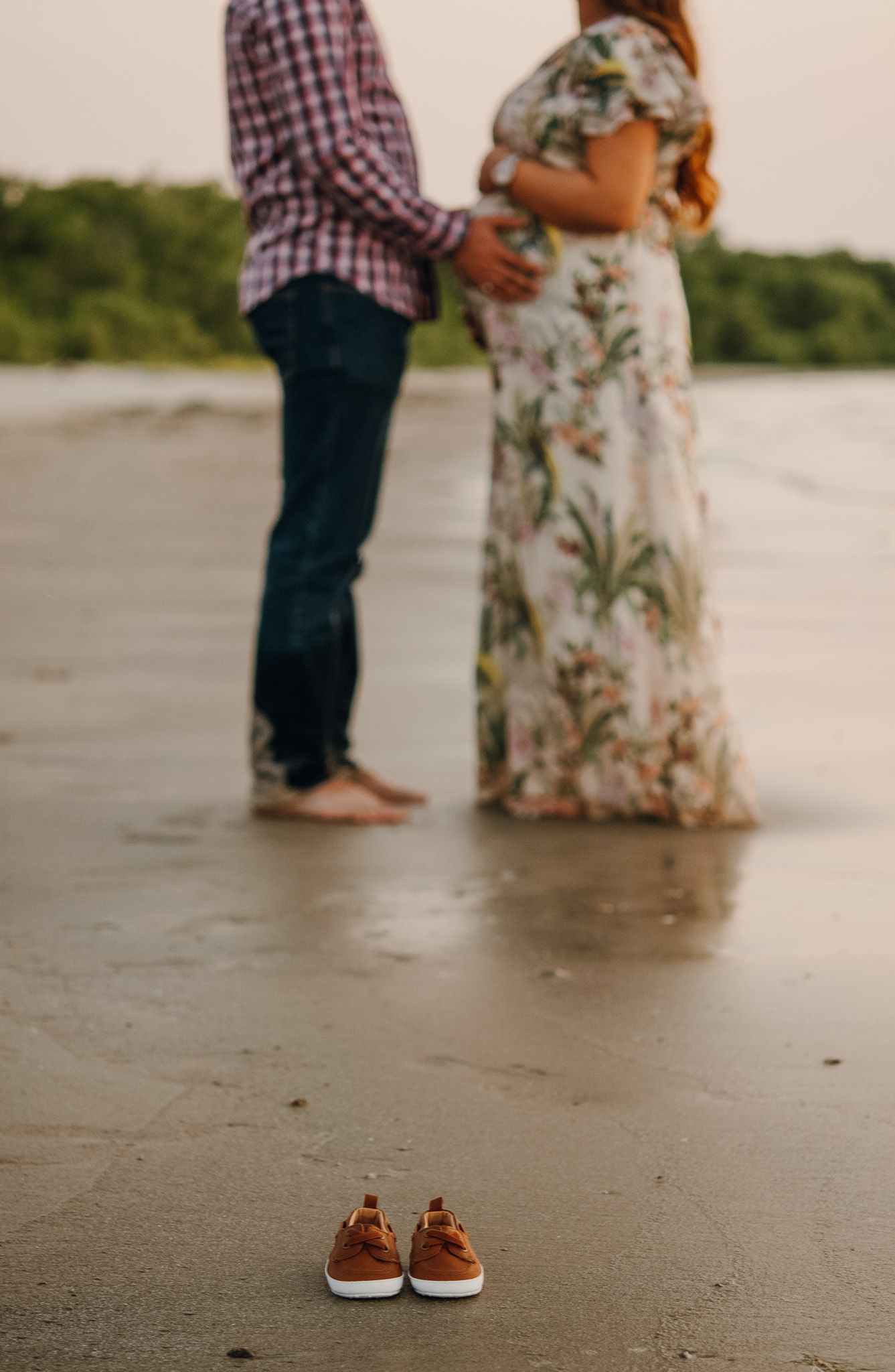 Couple holds pregnant womans belly on beach