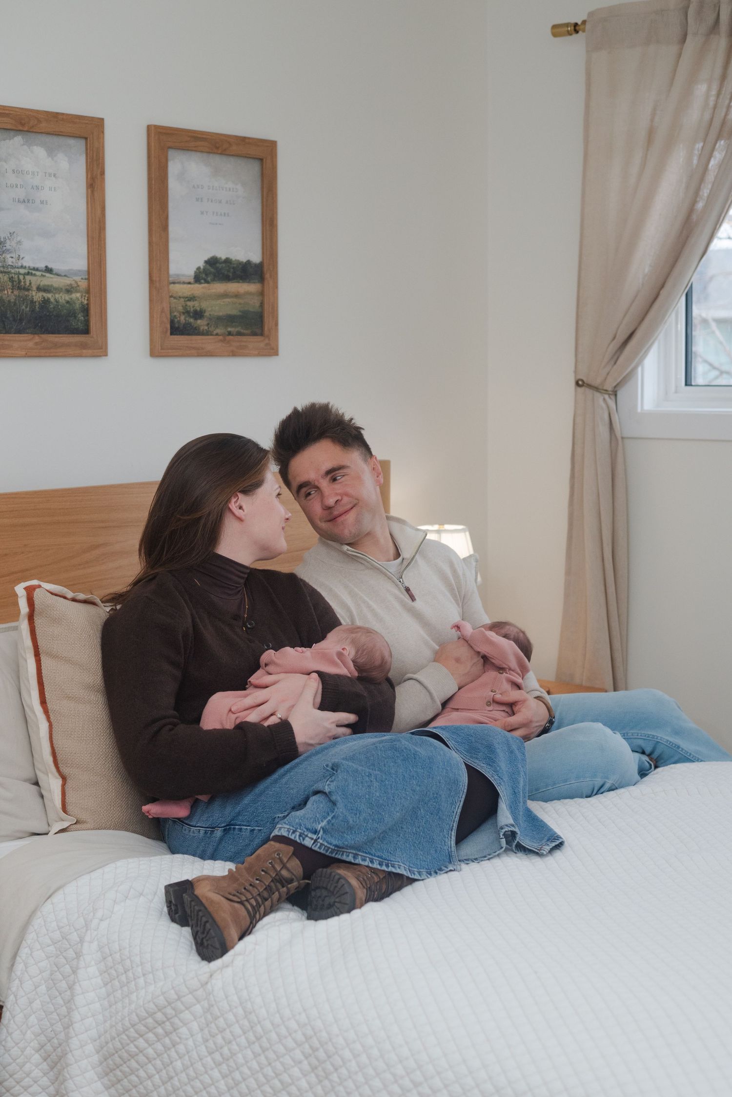 couple sits on bed, looking at each other holding their twins