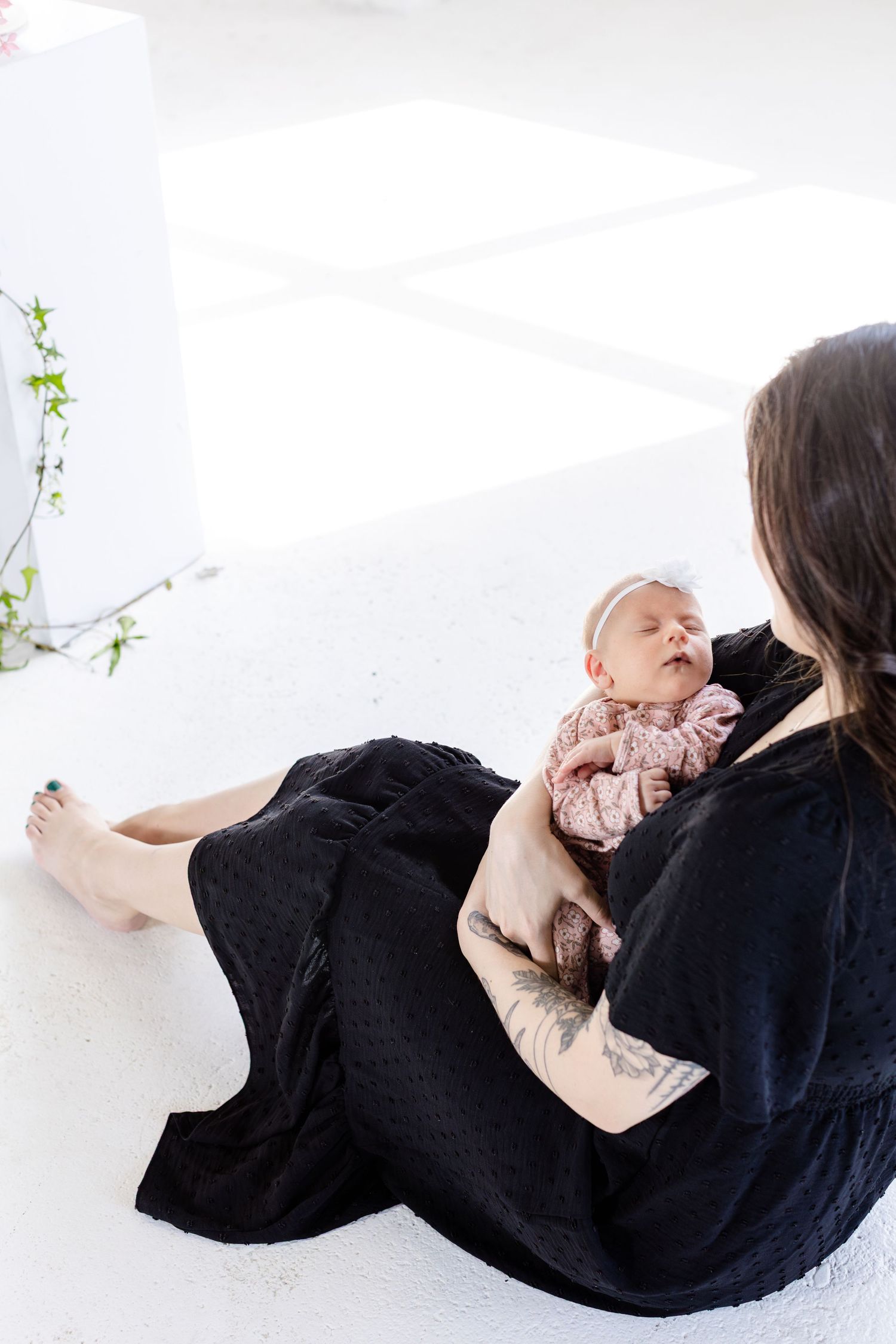 Mother wearing black dress with ling dark brown hair holding baby in pink clothes, in professional photo studio in Winnipeg for mothers  day