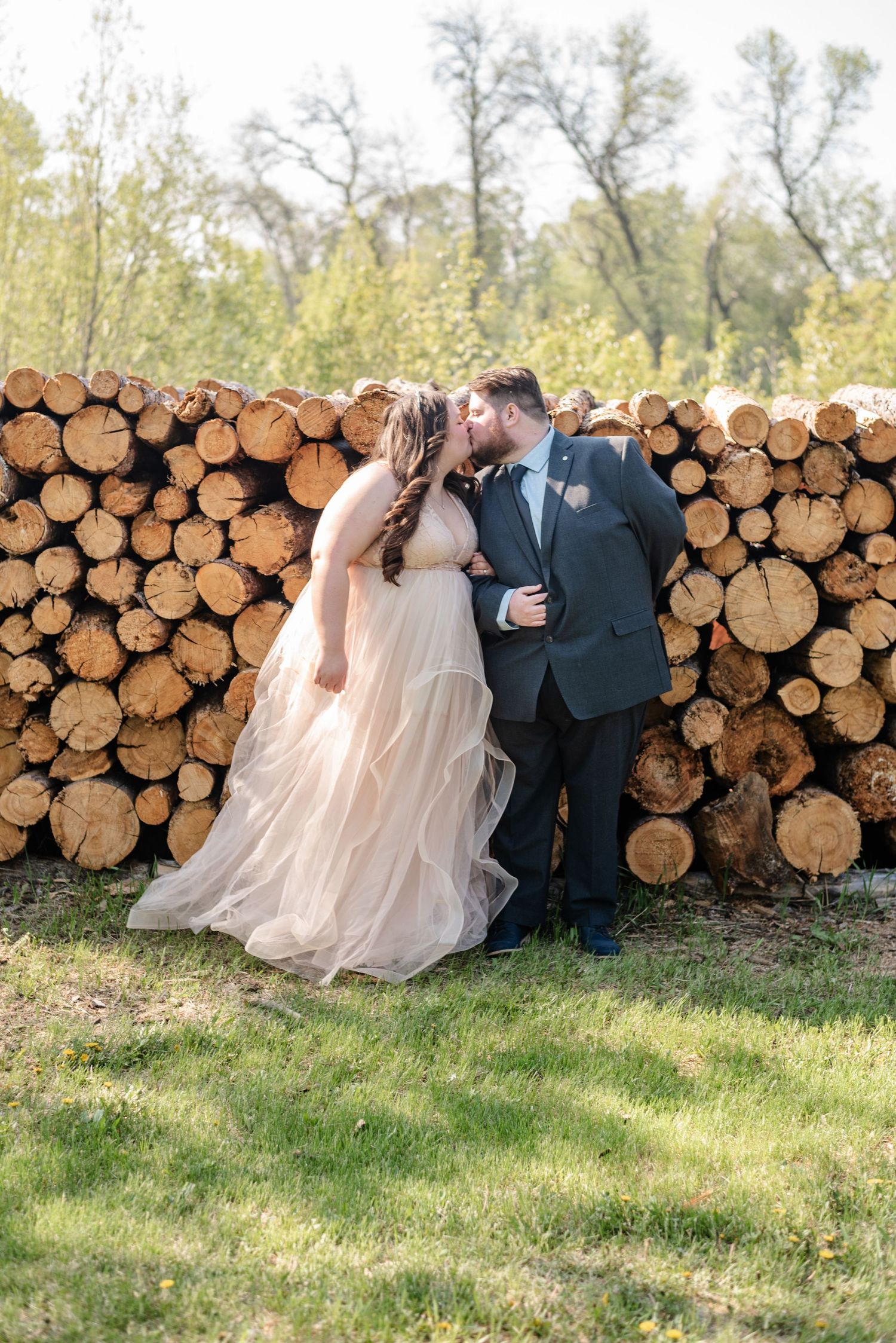 bride and groom kiss against wood pile