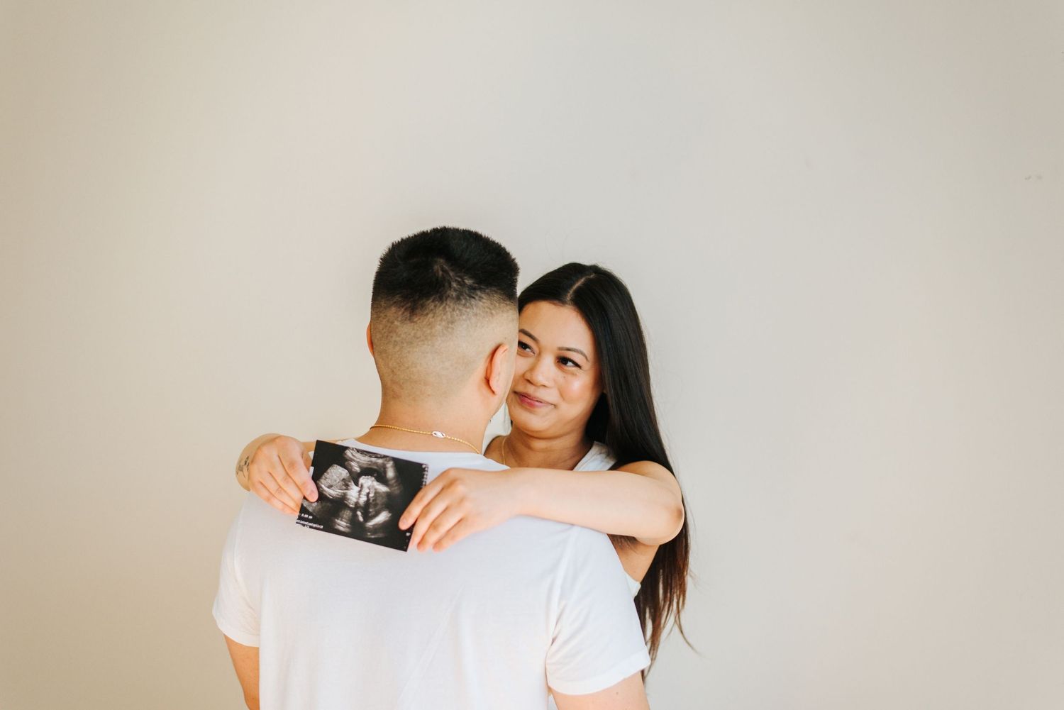 Couple look into eachother eyes holding sonogram